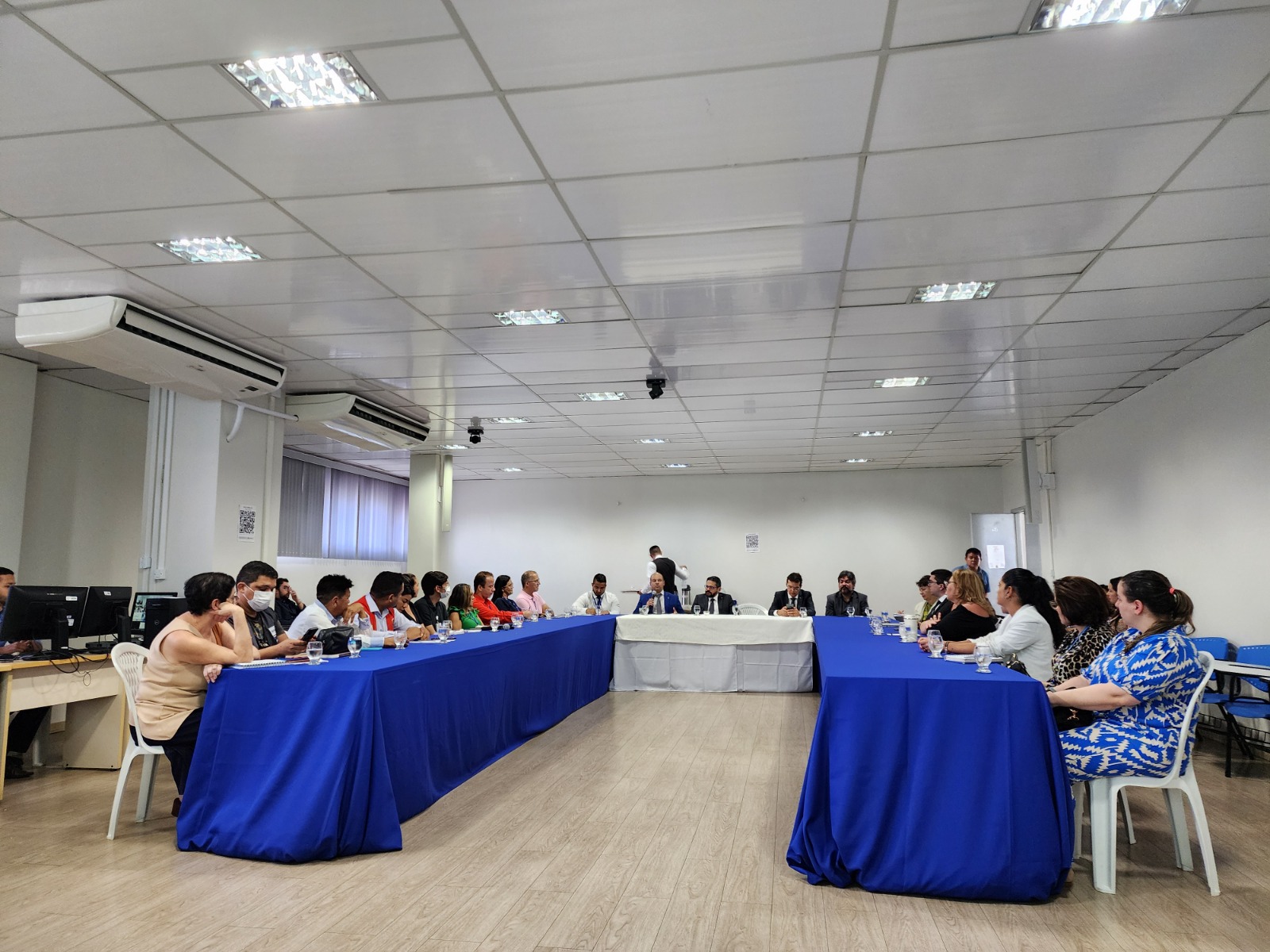 Foto colorida mostrando pessoas sentadas em frente a uma mesa de reunião.