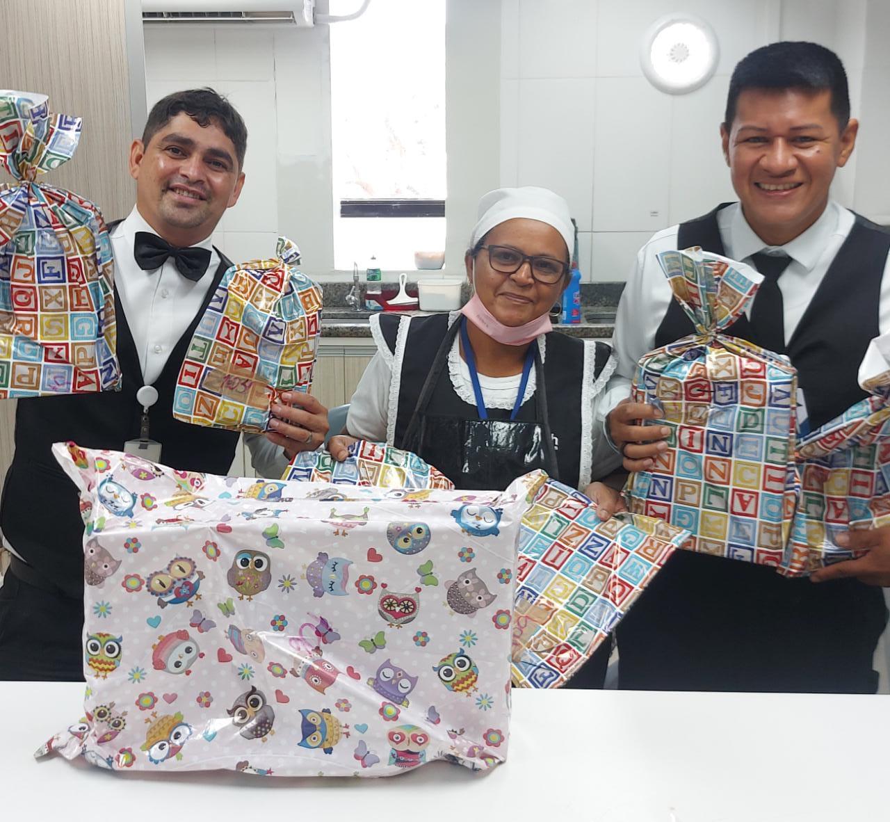 Foto colorida mostrando três pessoas segurando presentes embalados