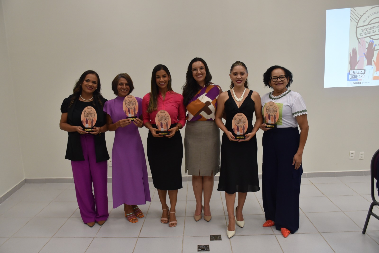 Foto colorida mostra 6 pessoas posando para foto segurando o Selo Mulheres Seguras.