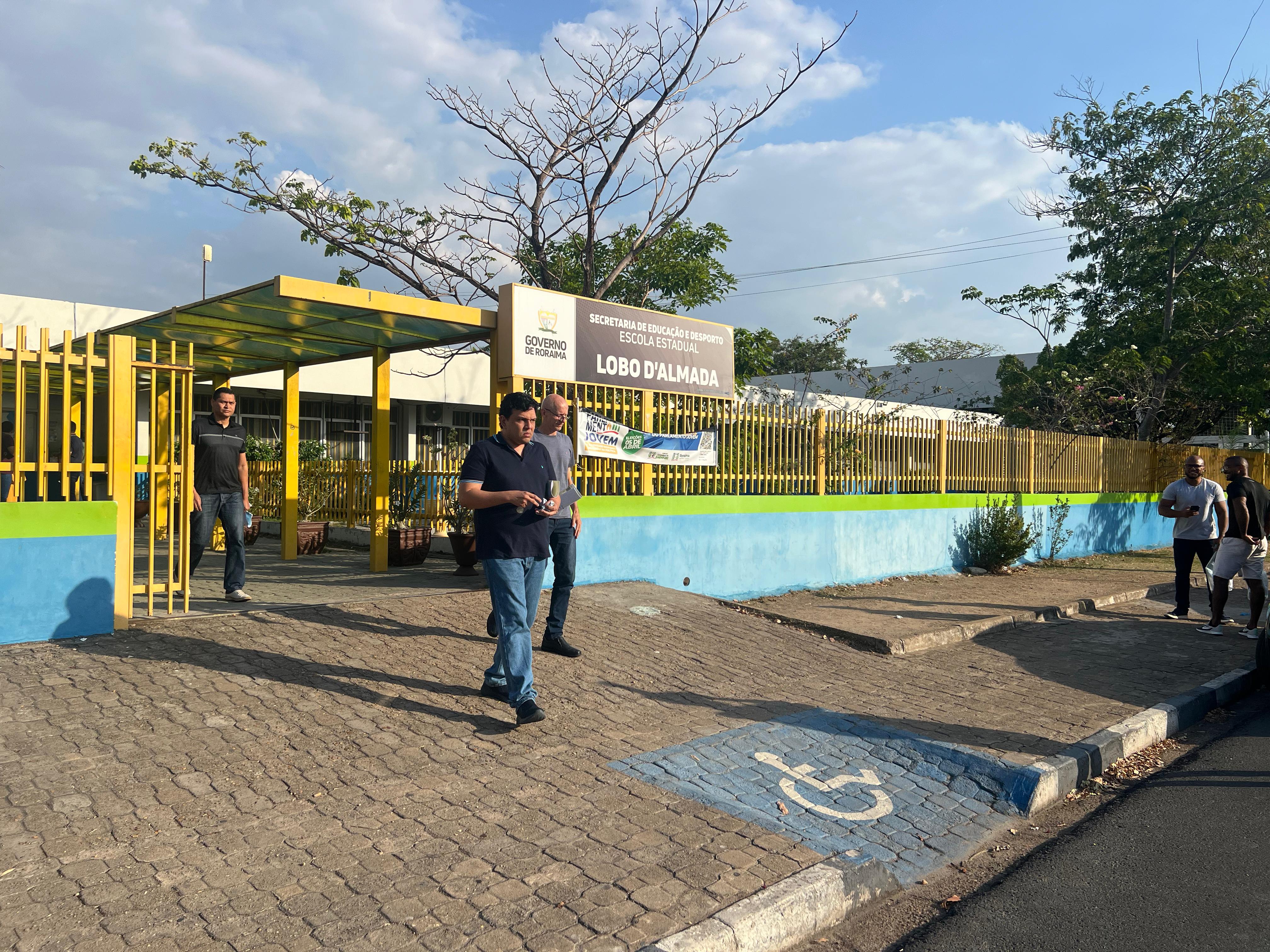 foto colorida da frente da Escola Lobo D'Almada , mostra três pessoas saindo da escola