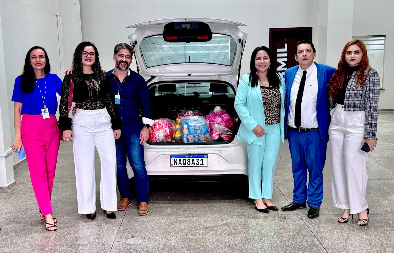 Foto colorida mostrando o o presidente do Tribunal de Justiça de Roraima, desembargador Jésus Nascimento, ao lado de 5 servidores da presidência, posando para foto. No meio um carro com o porta malas aberto e diversos produtos alimentícios