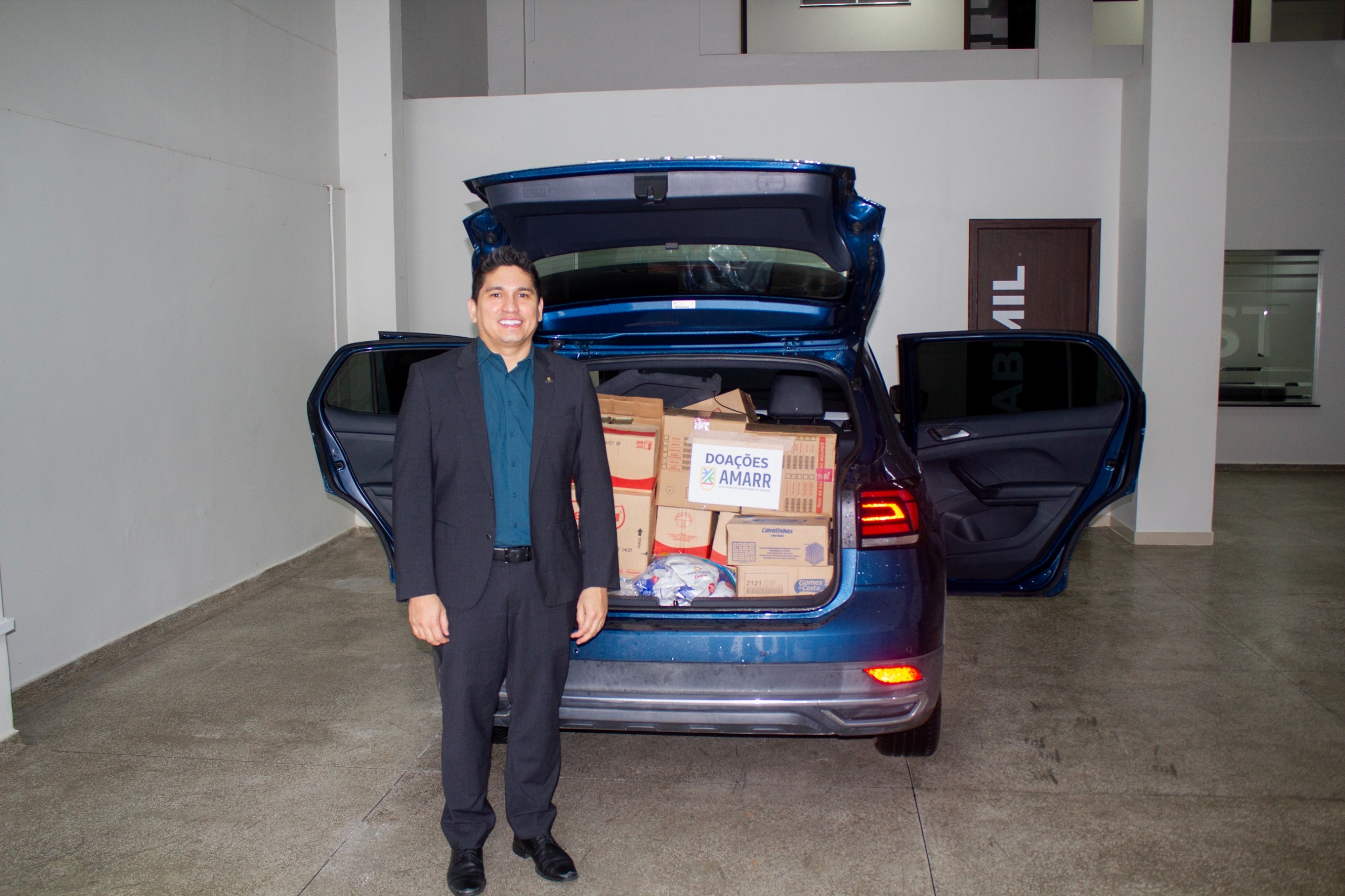 Juiz Marcelo Oliveira posando para foto. Atrás dele um carro como porta malas aberto e produtos alimentício dentro