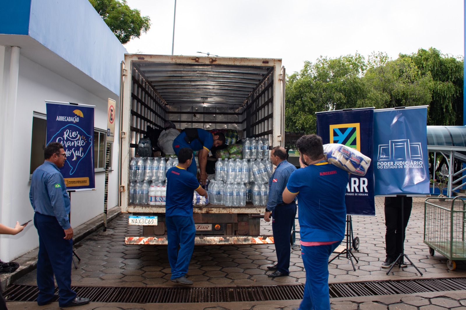 Foto colorida mostrando homens carregando fardos de garrafas de água para um caminhão