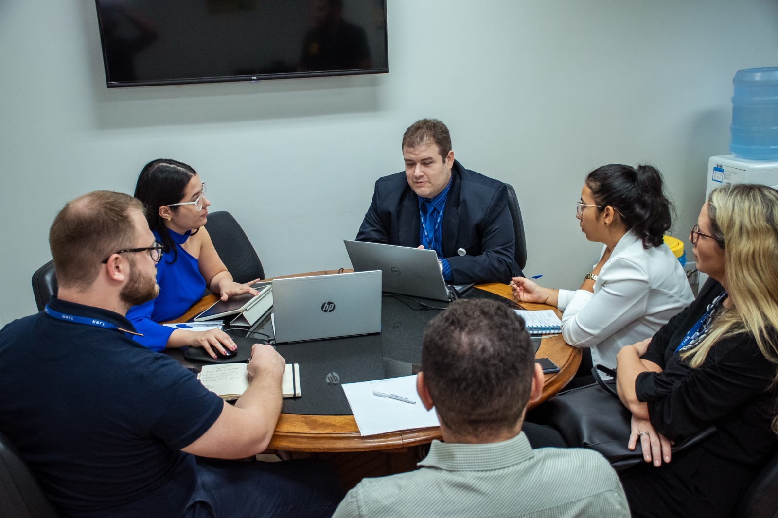 Foto colorida mostrando seis pessoas sentadas em frente a uma mesa redonda durante reunião