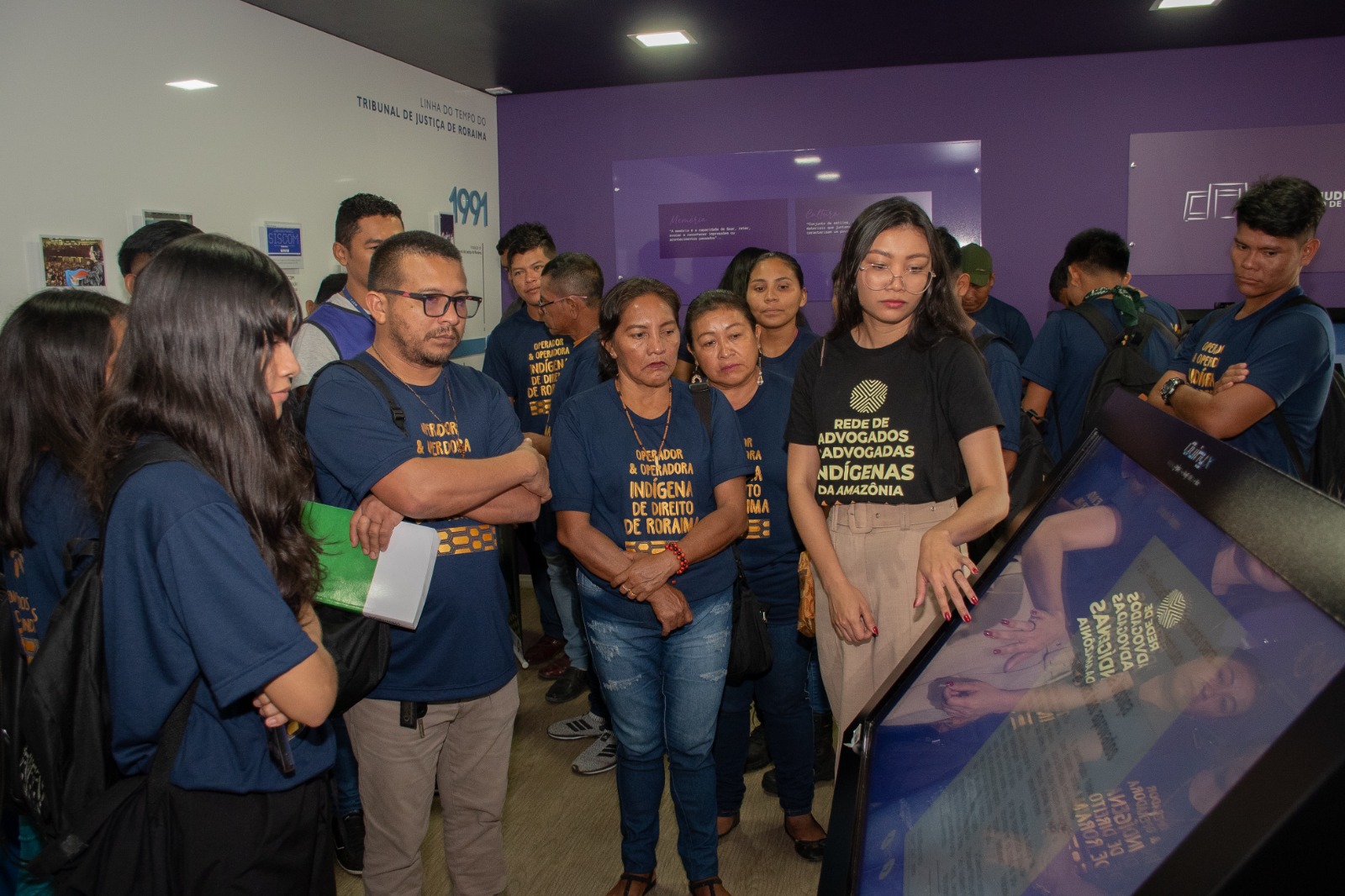 Foto colorida mostyrando pessoas olhando para um dos totens interativos do Centro de Memória durante visita ao local