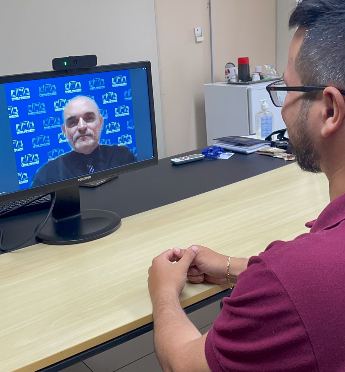 Foto colorida de cidadão realizando audiência online com juiz.