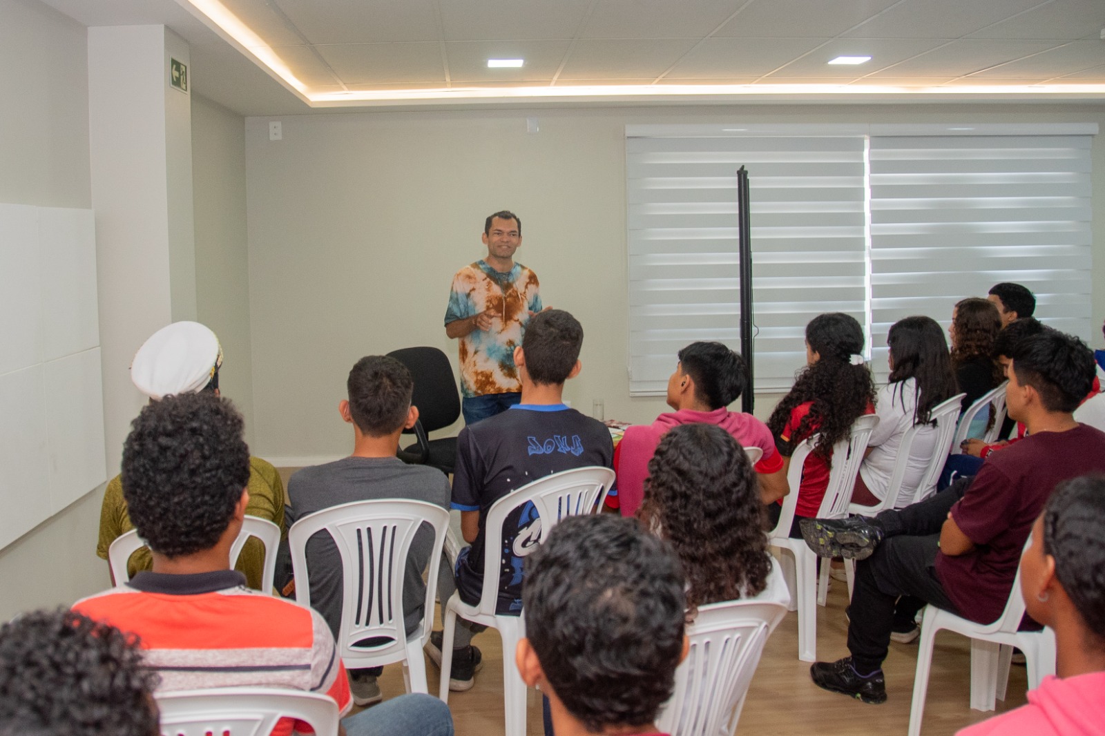 A imagem colorida mostra o autor e jornalista local, Aldenor Pimentel, em momento de palestra sobre suas obras e a cultura regional para alunos do ensino médio que prestigiaram o evento. Abaixo a frase: PRESERVANDO A CULTURA - mãos que escrevem a nossa história é tema do 2° festival de memória e cultura de Roraima