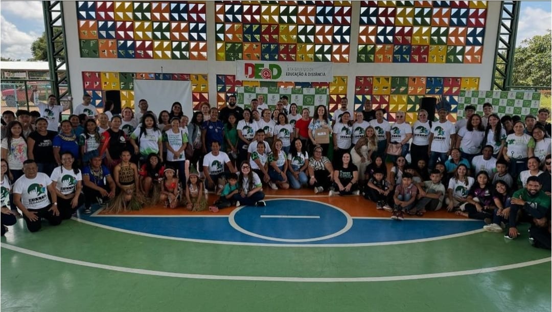Foto colorida mostra aproximadamente 60 pessoas em ginásio de escola posando para a foto. entre elas, estudantes, professores, servidores do TJRR