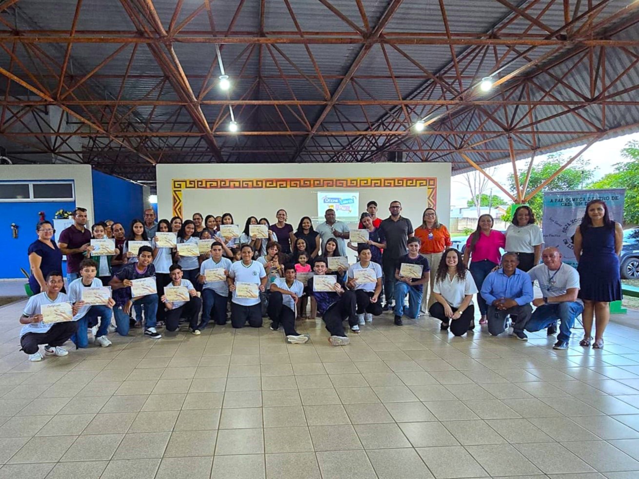 Foto colorida mostra aproximadamente 35 pessoas posando para a foto em uma escola. entre elas, estudantes, professores, servidores do TJRR 