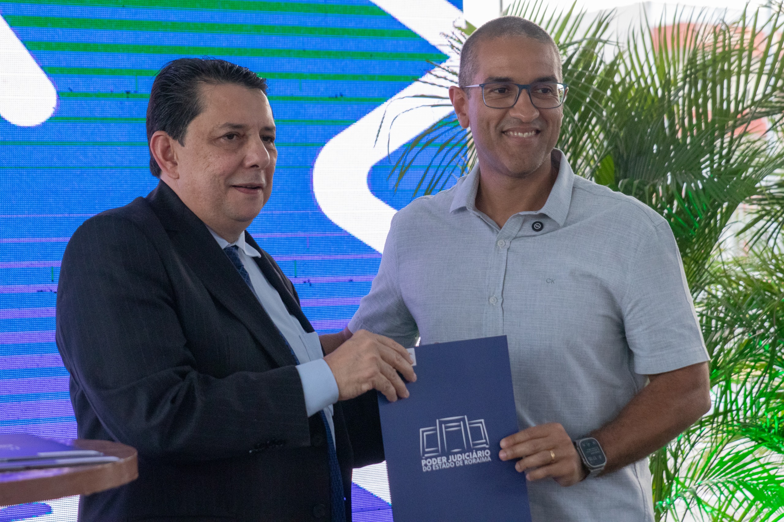 Imagem colorida contém o presidente do Tribunal de Justiça de Roraima (TJRR), desembargador Jésus Nascimento posando para fotografia ao lado do prefeito de Boa Vista, Arthur Henrique, enquanto seguram termo de adesão ao espaço no Fórum da Cidadania, durante inauguração que ocorreu no dia 12 de dezembro de 2024.