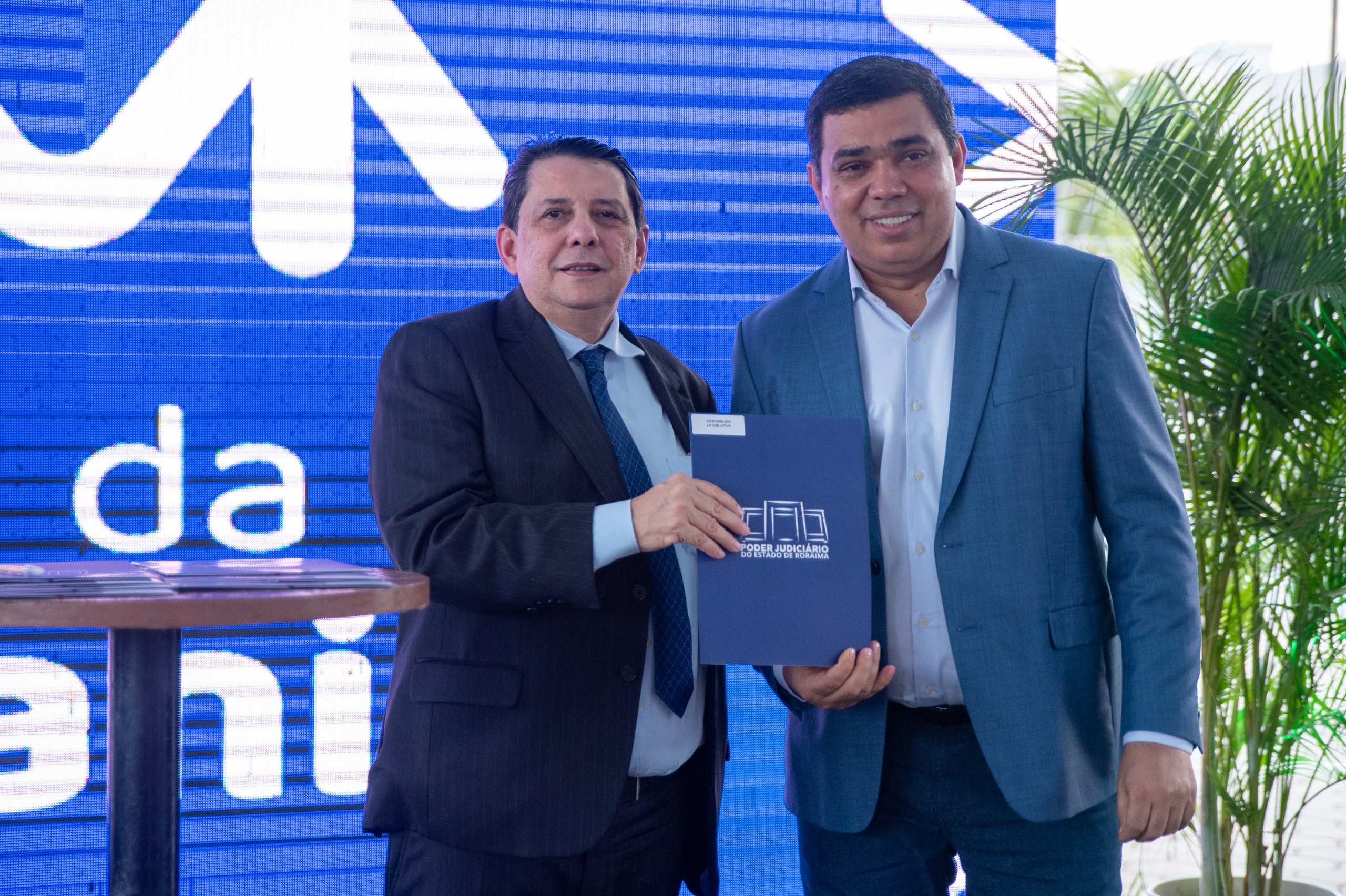 Imagem colorida contém o presidente do Tribunal de Justiça de Roraima (TJRR), desembargador Jésus Nascimento posando para fotografia ao lado do presidente da Assembleia Legislativa de Roraima, Soldado Sampaio, enquanto seguram termo de adesão ao espaço no Fórum da Cidadania, durante inauguração que ocorreu no dia 12 de dezembro de 2024.