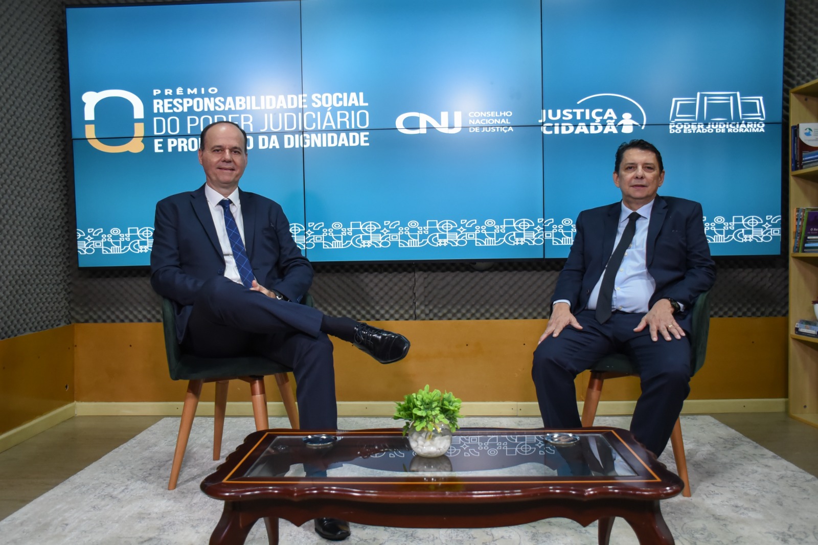 Imagem colorida mostra presidente do Tribunal de Justiça de Roraima, desembargador Jésus Nascimento sentado ao lado do coordenador do programa Justiça Cidadã, desembargador Cristóvão Suter, posando para foto.