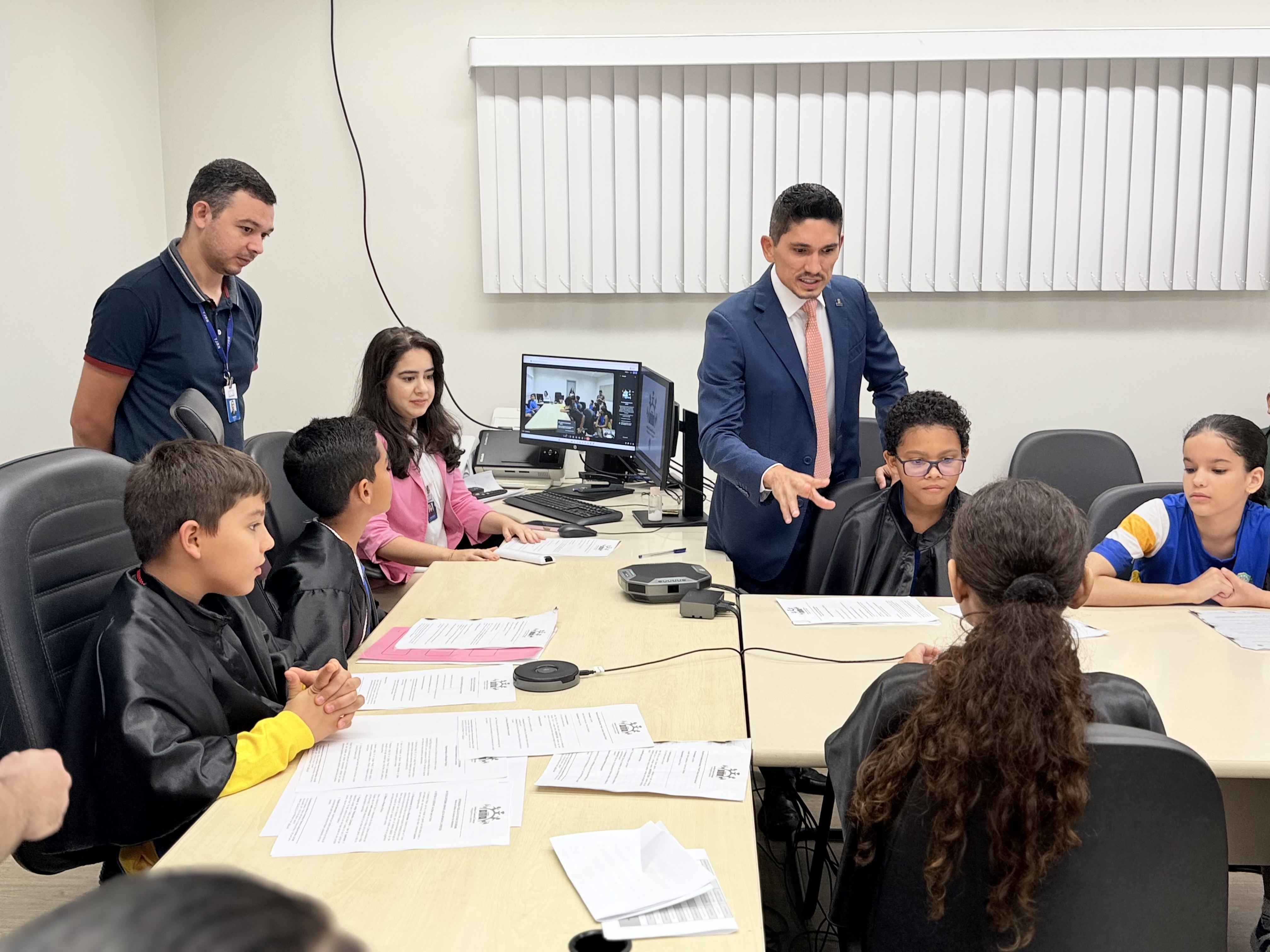 Imagem colorida mostra o juiz e coordenador da CIJ/TJRR, Marcelo Oliveira conversando com crianças, durante audiência simulada com crianças da Escola. Municipal