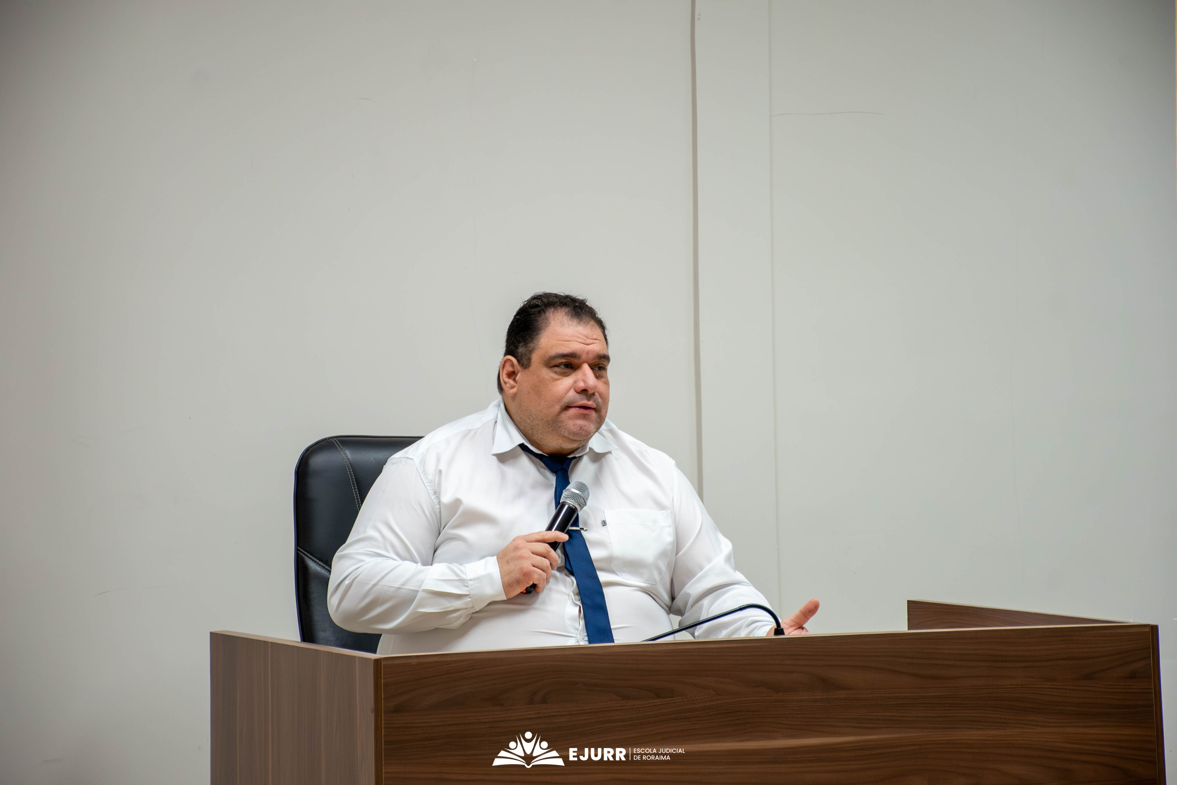 O magistrado da Comarca, Dr. Raimundo Anastácio, vestindo camisa social branca e gravata azul fala ao microfone, sentado atrás de uma bancada de madeira escura e gesticulando com a mão esquerda. O magistrado da Comarca, Dr. Raimundo Anastácio, vestindo camisa social branca e gravata azul fala ao microfone, sentado atrás de uma bancada de madeira escura e gesticulando com a mão esquerda.