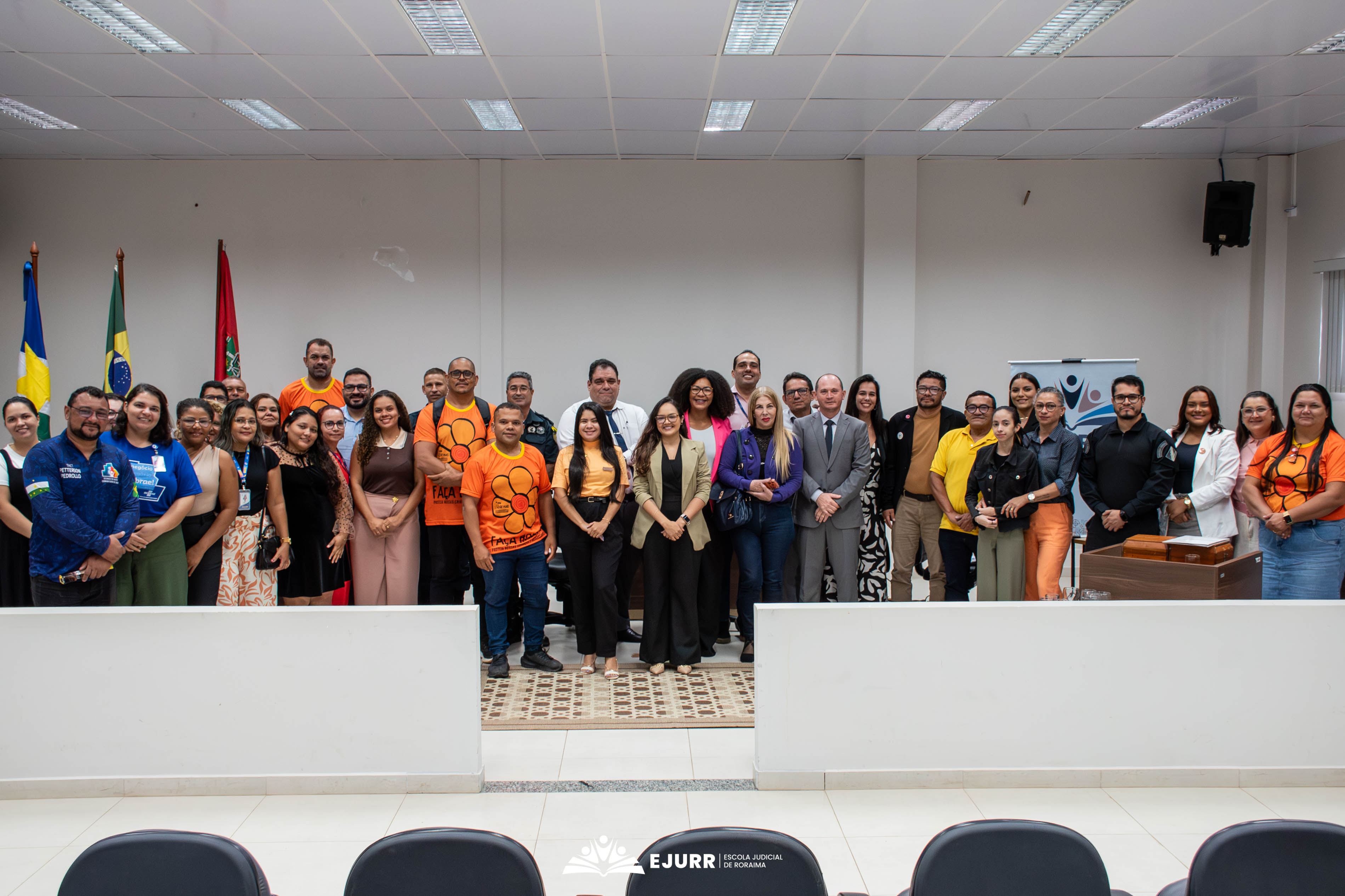 Foto oficial de encerramento reunindo dezenas de participantes de pé no palco do auditório. Várias pessoas no grupo vestem camisetas laranjas com a estampa de uma flor, símbolo da campanha de combate ao abuso infantil (Maio Laranja). À esquerda, aparecem as bandeiras oficiais hasteadas. Foto oficial de encerramento reunindo dezenas de participantes de pé no palco do auditório. Várias pessoas no grupo vestem camisetas laranjas com a estampa de uma flor, símbolo da campanha de combate ao abuso infantil (Maio Laranja). À esquerda, aparecem as bandeiras oficiais hasteadas.