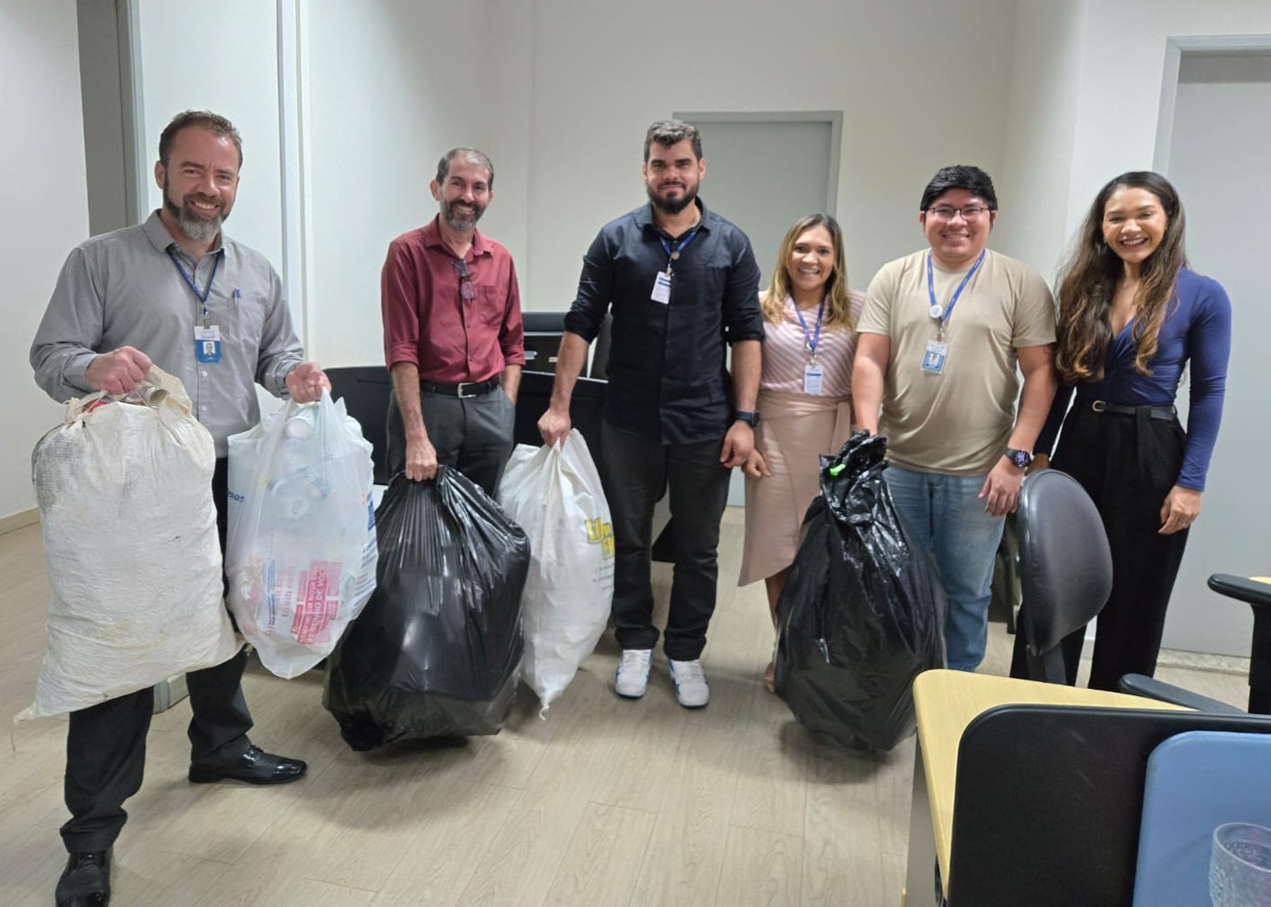Foto colorida mostra servidores posando em uma sala, segurando sacolas grandes com materiais coletados para descarte ou reciclagem. O grupo aparece sorrindo, com crachás institucionais, em um ambiente interno do Tribunal de Justiça de Roraima. Foto colorida mostra servidores posando em uma sala, segurando sacolas grandes com materiais coletados para descarte ou reciclagem. O grupo aparece sorrindo, com crachás institucionais, em um ambiente interno do Tribunal de Justiça de Roraima.