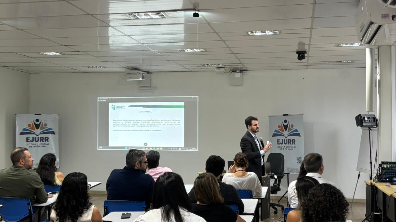 homem falando no microfone e gesticulando para um grupo de pessoas sentadas 