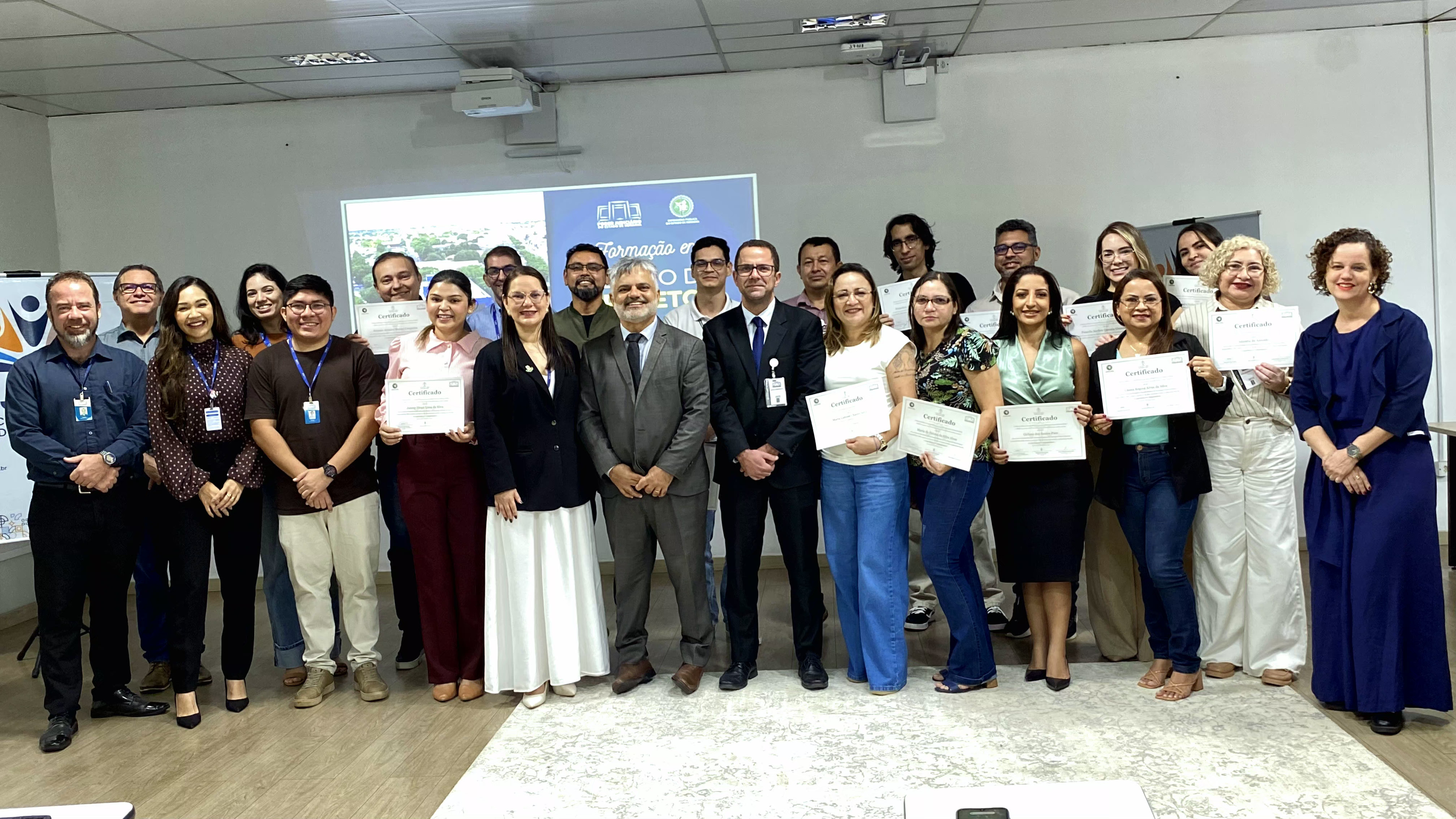 Foto em grupo dos participantes reunidos lado a lado. Eles sorriem para a câmera e vários seguram certificados brancos nas mãos.