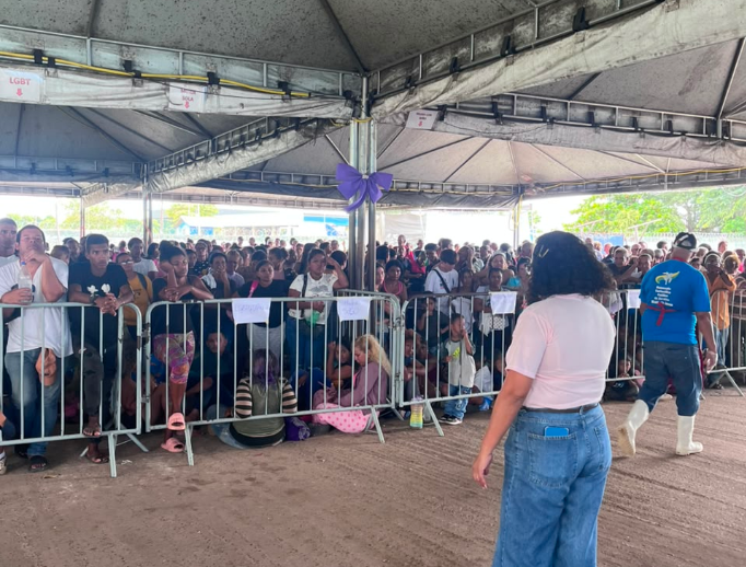 ultidão reunida sob uma tenda, com pessoas sentadas e outras em pé, aguardando atendimento ou evento, criando uma atmosfera de expectativa. multidão reunida sob uma tenda, com pessoas sentadas e outras em pé, aguardando atendimento ou evento, criando uma atmosfera de expectativa.