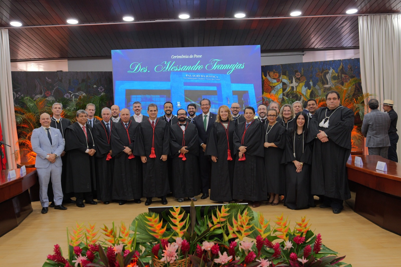  Imagem colorida mostra grupo de magistrados e autoridades posando para foto oficial no palco, diante do painel da cerimônia de posse e da decoração com arranjos florais.