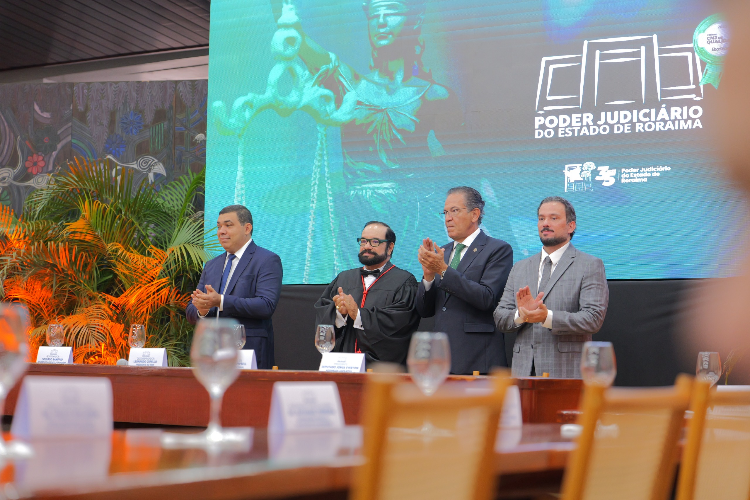 Imagem colorida registra autoridades dos Três Poderes de Roraima  o presidente do TJRR, desembargador Leonardo Cupello, o governador Soldado Sampaioe o presidente da Assembleia Legislativa de Roraima, deputado Jorge Everton, ao lado do ministro do STJ Mauro Campbell, durante momento de aplausos na sessão solene de posse do desembargador Alessandro Tramujas