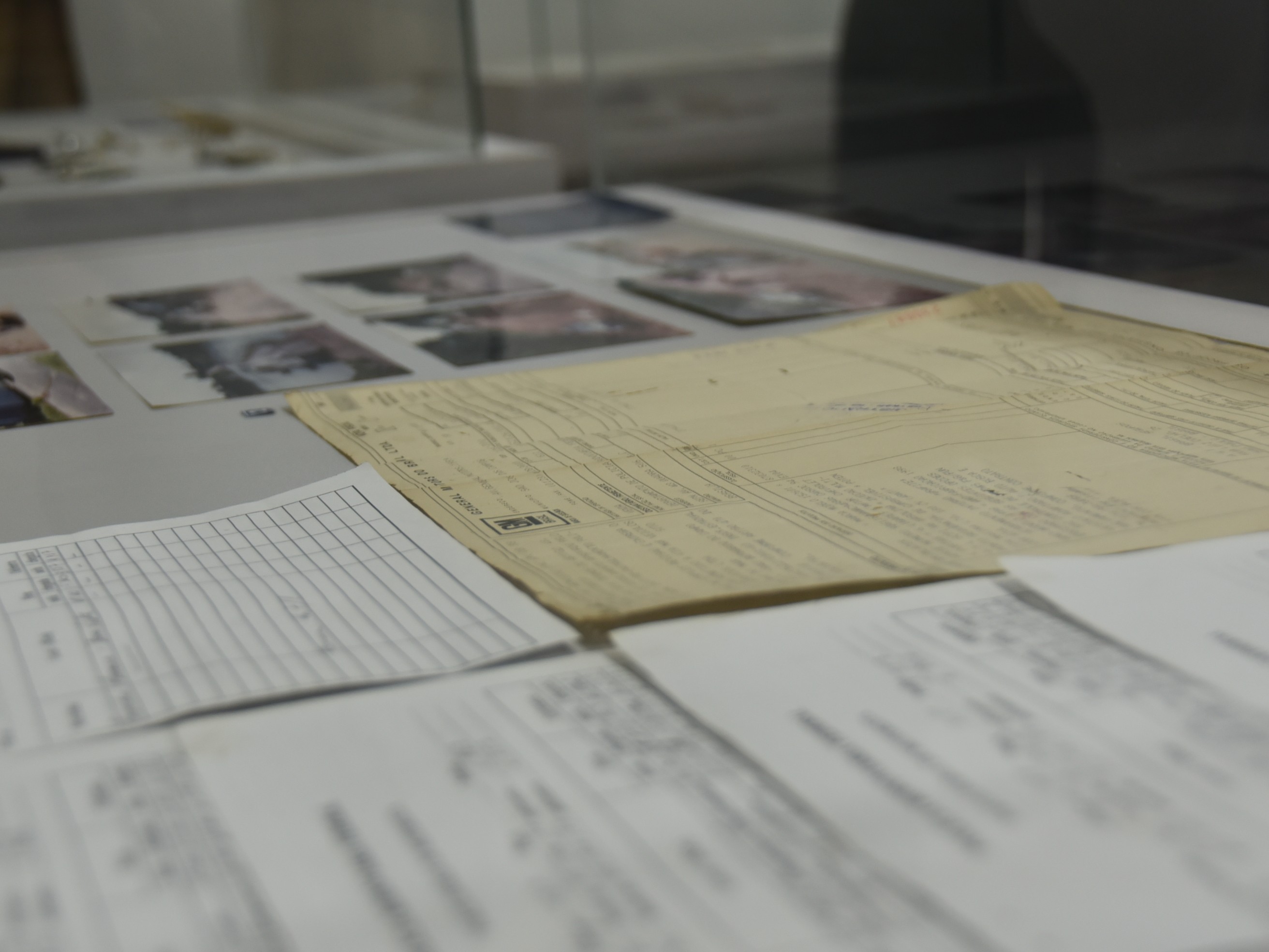 Imagem colorida mostra documentos, formulários e fotografias antigas preservados em uma das vitrines da exposição, compondo o acervo histórico da atuação da PRF no estado.