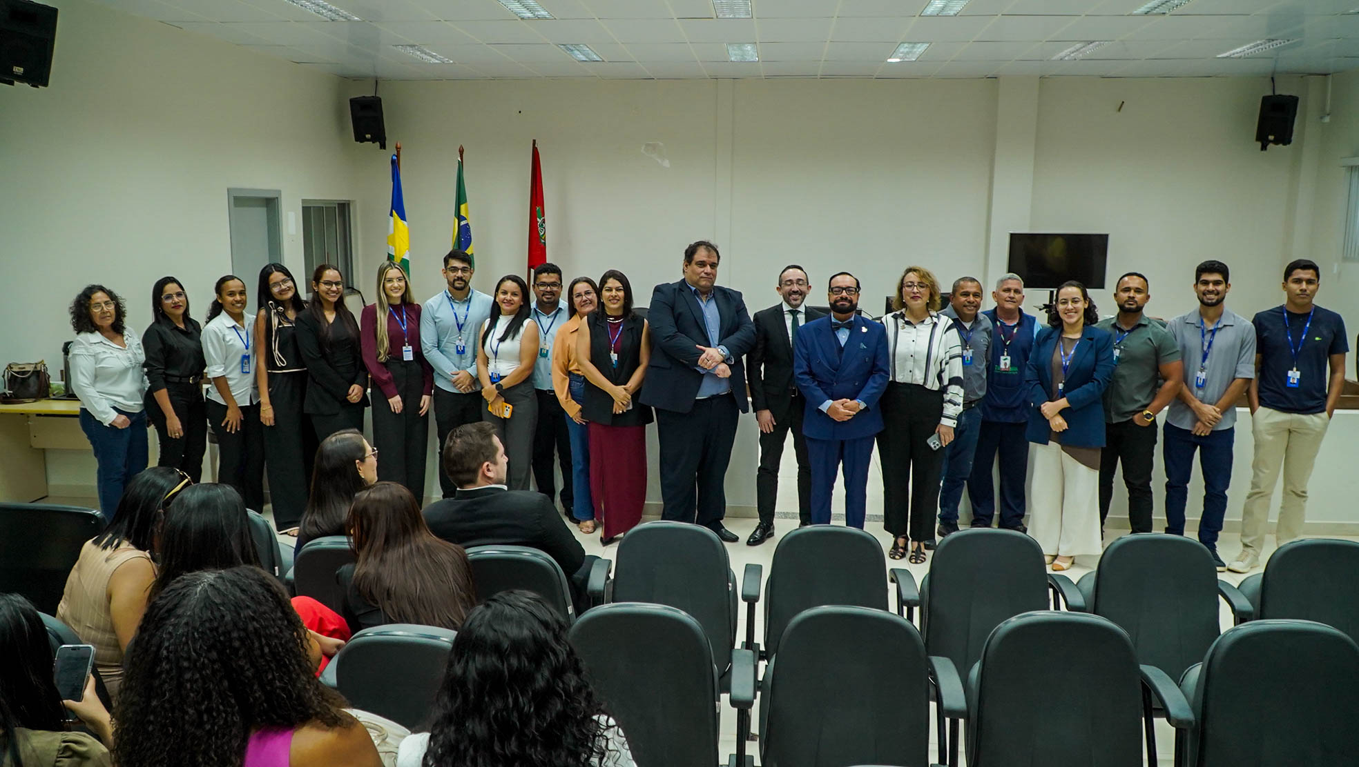 Imagem colorida mostra magistrados, servidores e integrantes da comitiva administrativa posando para uma fotografia coletiva no auditório da unidade, com bandeiras ao fundo.