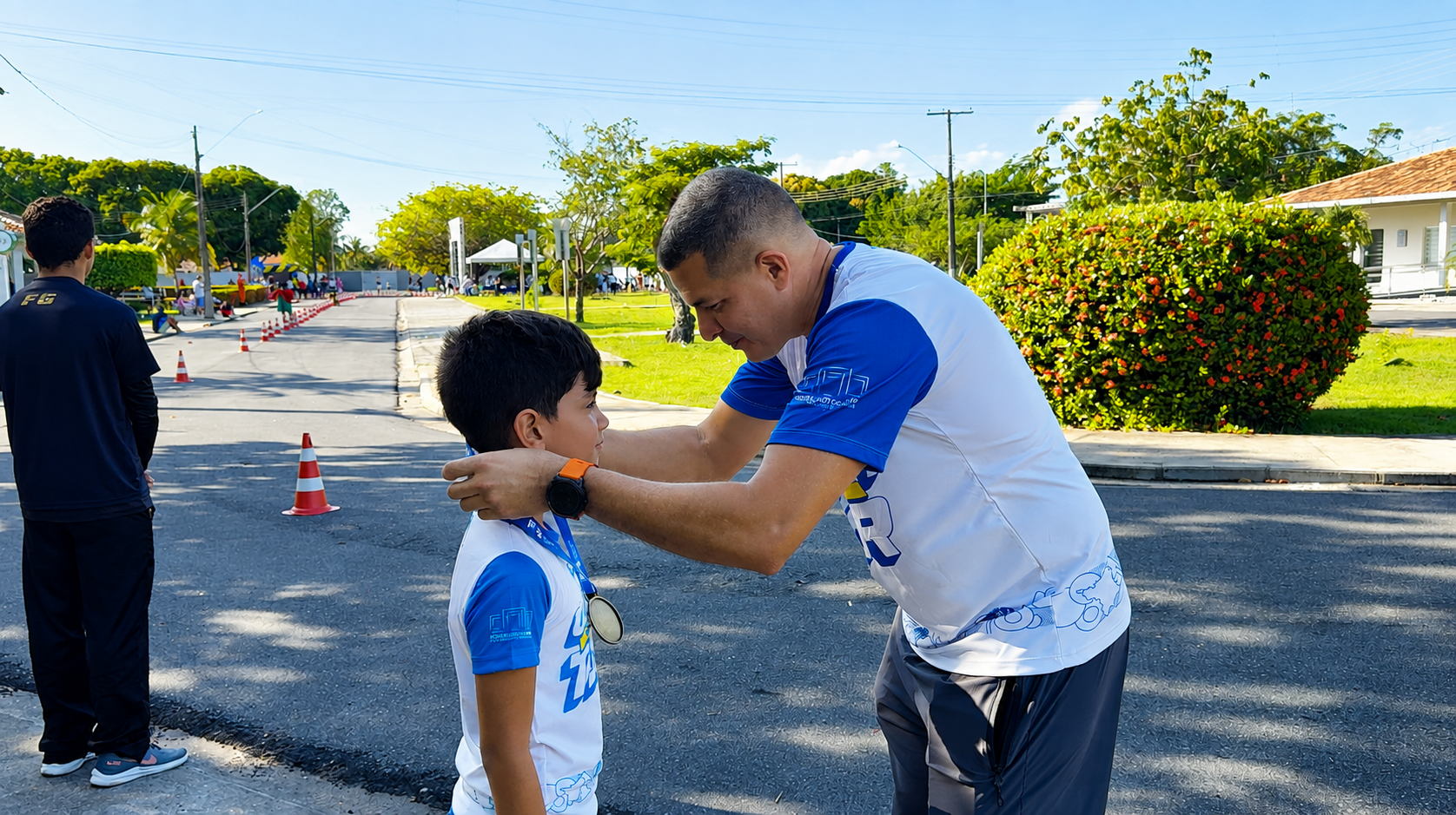 Imagem colorida registra um menino recebendo uma medalha após participar da Corrida Kids. Um homem coloca a medalha no pescoço da criança, em trecho do percurso montado nas dependências do Complexo Sociocultural. Imagem colorida registra um menino recebendo uma medalha após participar da Corrida Kids. Um homem coloca a medalha no pescoço da criança, em trecho do percurso montado nas dependências do Complexo Sociocultural.
