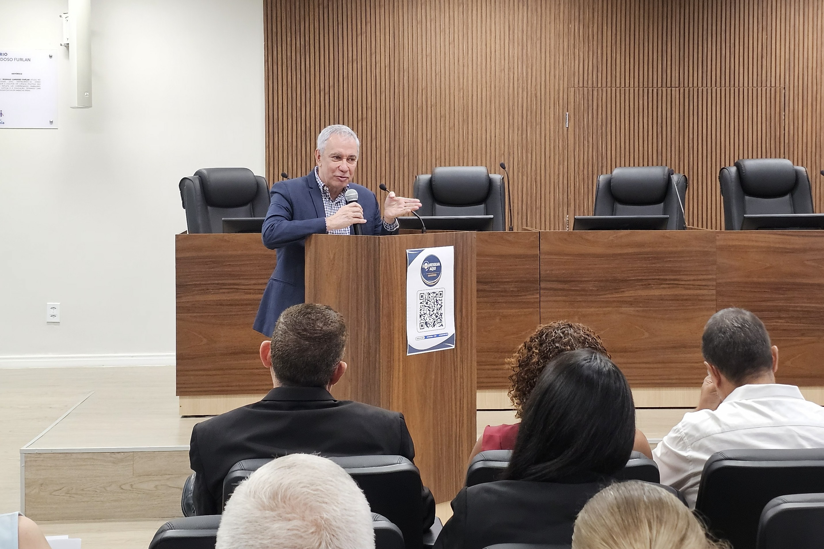 Imagem colorida registra a apresentação do balanço da III Ação Sociojurídica de Atendimento à Pessoa Encarcerada. Um homem fala ao microfone diante do público, enquanto uma tela ao fundo exibe informações sobre a iniciativa. Representantes de instituições parceiras e integrantes das forças de segurança acompanham a exposição. Imagem colorida registra a apresentação do balanço da III Ação Sociojurídica de Atendimento à Pessoa Encarcerada. Um homem fala ao microfone diante do público, enquanto uma tela ao fundo exibe informações sobre a iniciativa. Representantes de instituições parceiras e integrantes das forças de segurança acompanham a exposição.