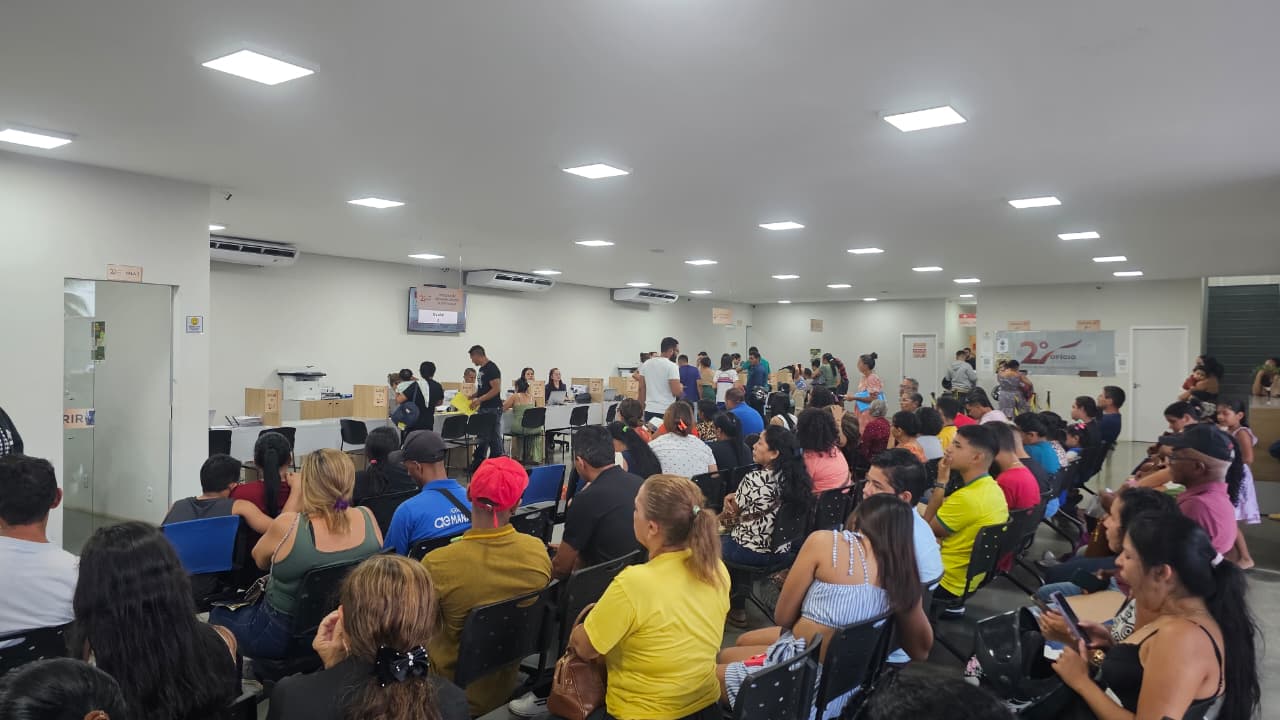 Imagem colorida mostra dezenas de pessoas aguardando atendimento durante o mutirão para emissão da Carteira de Identidade Nacional. O público ocupa as cadeiras de uma ampla sala de espera, enquanto equipes trabalham em mesas de atendimento ao fundo.