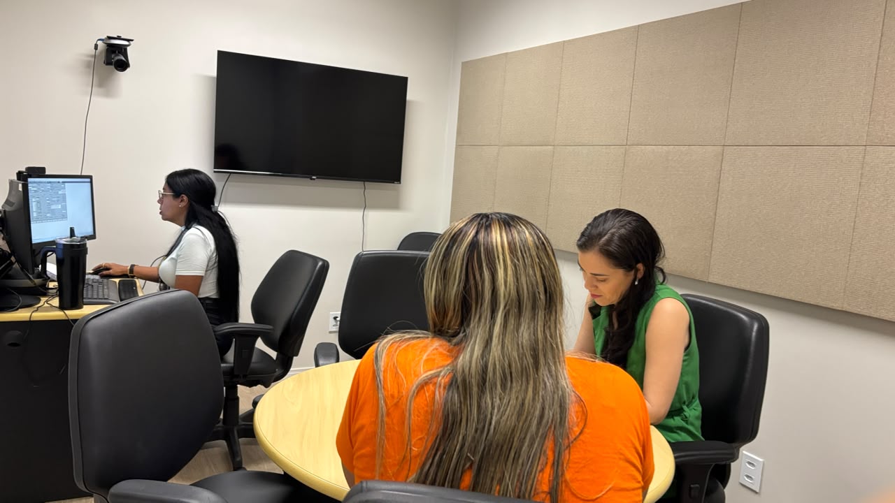 Imagem colorida mostra uma audiência de conciliação durante o mutirão para negociação de débitos com a Âmbar Energia. Duas mulheres conversam frente a frente em uma mesa de atendimento, enquanto outra profissional trabalha em um computador ao lado. Imagem colorida mostra uma audiência de conciliação durante o mutirão para negociação de débitos com a Âmbar Energia. Duas mulheres conversam frente a frente em uma mesa de atendimento, enquanto outra profissional trabalha em um computador ao lado.Imagem colorida mostra uma audiência de conciliação durante o mutirão para negociação de débitos com a Âmbar Energia. Duas mulheres conversam frente a frente em uma mesa de atendimento, enquanto outra profissional trabalha em um computador ao lado.