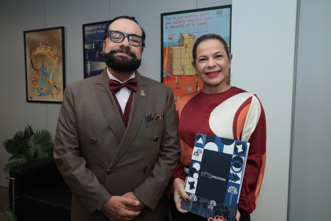 Imagem colorida mostra o Presidente do TJRR, desembargador Leonardo Cupello, e a conselheira do CNJ Noemia Porto, posando lado a lado em um ambiente interno. A conselheira segura a 4ª Edição da Revista do Poder Judiciário Roraimense Imagem colorida mostra o Presidente do TJRR, desembargador Leonardo Cupello, e a conselheira do CNJ Noemia Porto, posando lado a lado em um ambiente interno. A conselheira segura a 4ª Edição da Revista do Poder Judiciário Roraimense