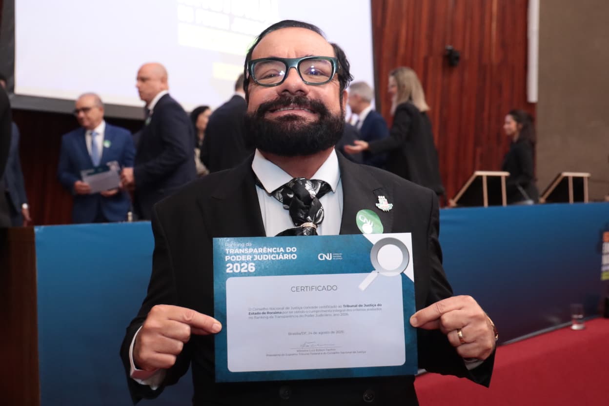 Imagem colorida mostra o Presidente do TJRR, desembargador Leonardo Cupello, vestindo terno preto e gravata estampada em preto e branco, sorrindo enquanto segura o certificado "Ranking da TRANSPARÊNCIA DO PODER JUDICIÁRIO 2026" do Conselho Nacional de Justiça Imagem colorida mostra o Presidente do TJRR, desembargador Leonardo Cupello, vestindo terno preto e gravata estampada em preto e branco, sorrindo enquanto segura o certificado "Ranking da TRANSPARÊNCIA DO PODER JUDICIÁRIO 2026" do Conselho Nacional de Justiça