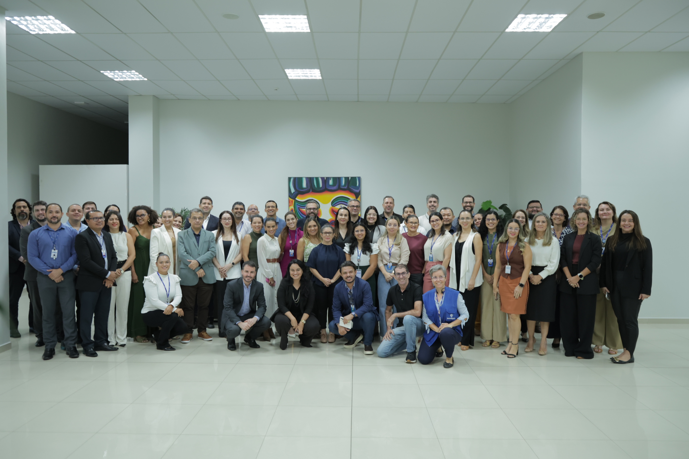 Fotografia mostra um grupo de pessoas reunido para uma foto coletiva em um ambiente interno. Os participantes estão organizados em diferentes fileiras, alguns em pé e outros agachados à frente. Fotografia mostra um grupo de pessoas reunido para uma foto coletiva em um ambiente interno. Os participantes estão organizados em diferentes fileiras, alguns em pé e outros agachados à frente.