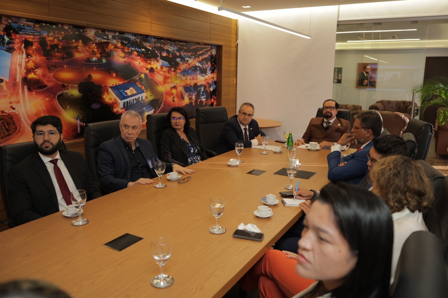  Imagem colorida registra reunião entre representantes do Judiciário e de instituições parceiras em uma sala institucional. O grupo está reunido ao redor de uma grande mesa de madeira, em momento de diálogo sobre a possível implantação do método APAC em Roraima.
