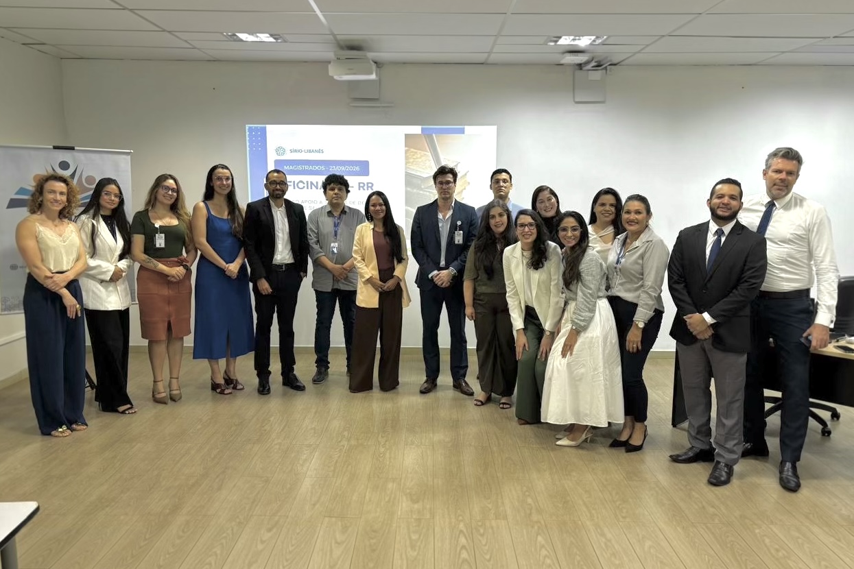 Foto 3: Fotografia colorida mostra um grupo de homens e mulheres em trajes esporte fino e social posados lado a lado no centro de uma sala de aula. Ao fundo, veem-se um banner da EJURR e a projeção de um slide na parede indicando o encerramento do evento. Fim da descrição.