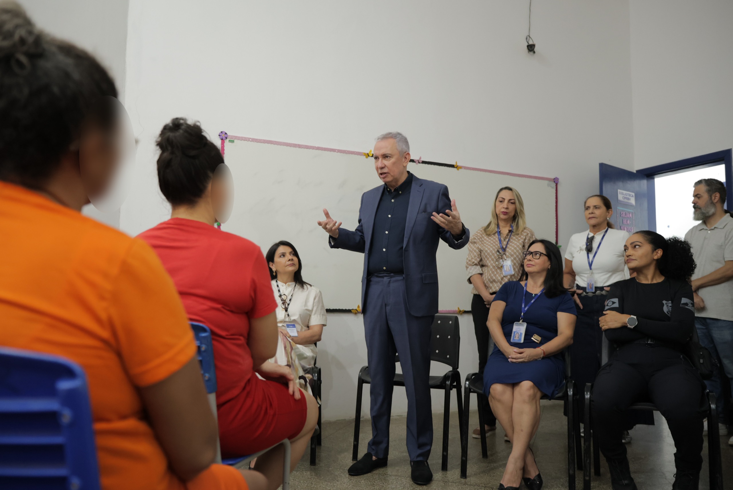 Reunião em sala: homem de cabelos grisalhos fala e gesticula diante de adultos sentados Reunião em sala: homem de cabelos grisalhos fala e gesticula diante de adultos sentados