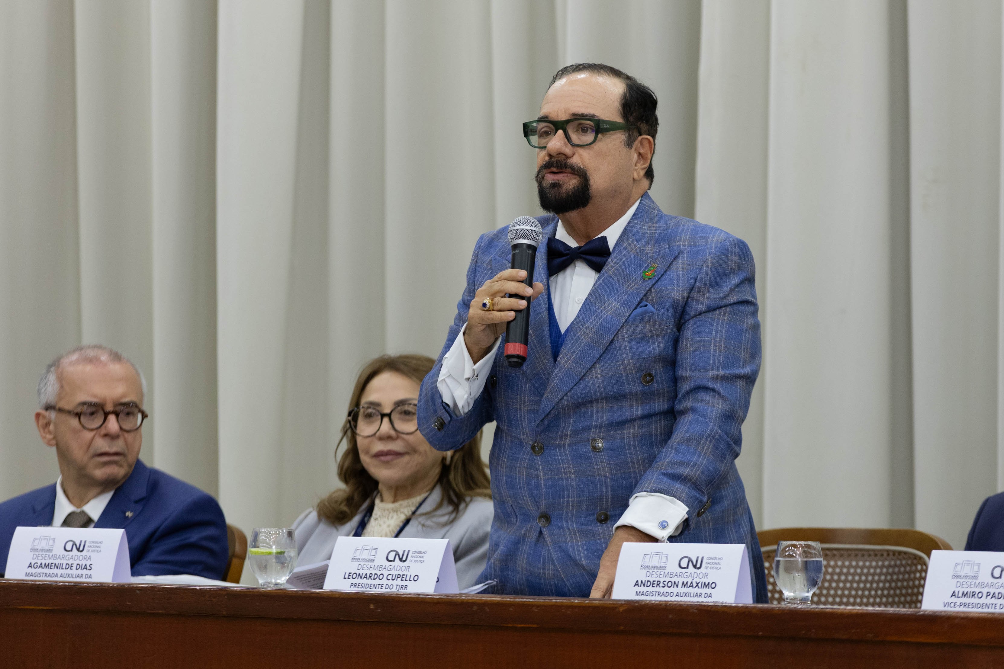 Imagem colorida registra o presidente do Tribunal de Justiça de Roraima durante pronunciamento na solenidade de encerramento da inspeção. Ele aparece em pé, segurando um microfone, diante da mesa de autoridades, enquanto outros participantes acompanham a fala. Imagem colorida registra o presidente do Tribunal de Justiça de Roraima durante pronunciamento na solenidade de encerramento da inspeção. Ele aparece em pé, segurando um microfone, diante da mesa de autoridades, enquanto outros participantes acompanham a fala.