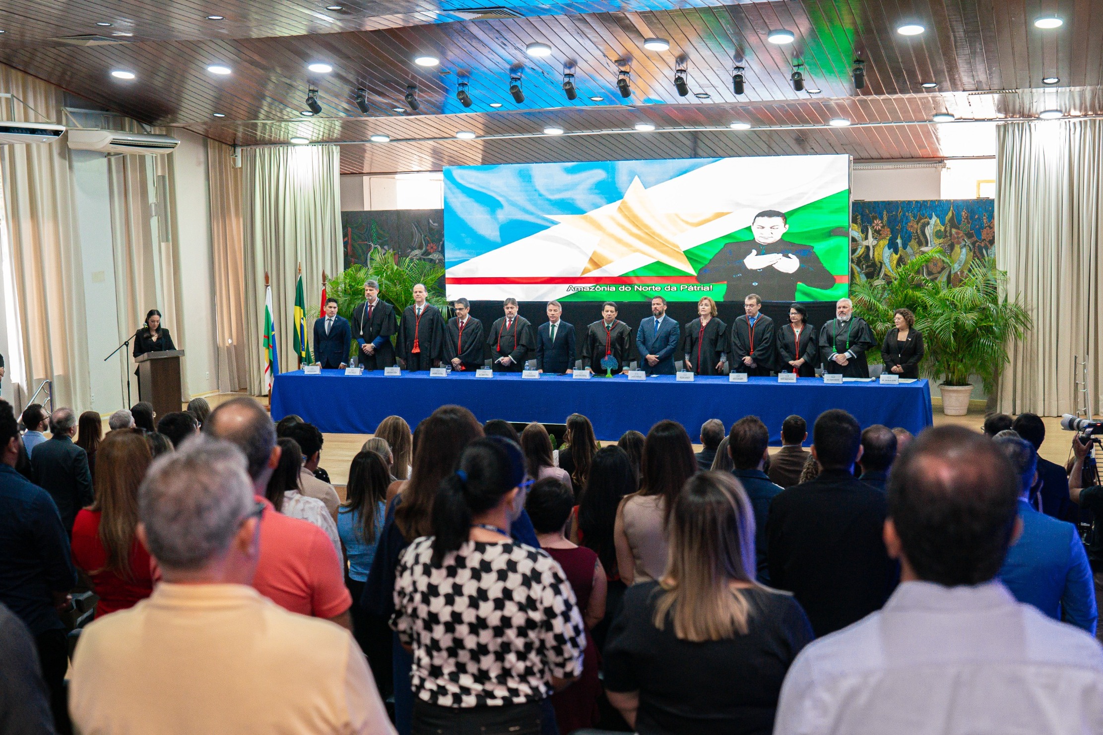 foto colorida mostra a solenidade de abertura do Ano Judiciário 2025 do Tribunal de Justiça de Roraima (TJRR). No palco, uma mesa com treze autoridades veste trajes formais e togas, enquanto uma mulher discursa em um púlpito. Da esquerda para a direita: o presidente da Associação de Magistrados do Estado de Roraima, Marcelo Oliveira; o juiz convocado, Luiz Fernando Mallet; o diretor da Escola Judicial de Roraima, desembargador Cristóvão Súter; o vice-presidente do Tribunal de Justiça de Roraima, desembargador Ricardo Oliveira; o procurador-geral de Justiça do Ministério Público de Roraima, Fábio Stica; o governador do Estado de Roraima, Antônio Denarium; o presidente do Tribunal de Justiça do Estado de Roraima, desembargador Jésus Nascimento; o vice-presidente da Assembleia Legislativa do Estado de Roraima, deputado Jorge Everton; a presidente do TRE-Roraima, desembargadora Elaine Bianchi; o ouvidor-geral de Justiça, desembargador Erick Linhares; a corregedora do TRE, desembargadora Tânia Vasconcelos; o defensor público-geral do Estado de Roraima, Dr. Oleno Matos; e a vice-presidente da Ordem dos Advogados do Brasil – Seccional Roraima, Dra. Natália Leitão Costa. Ao fundo, um telão exibe o logotipo do TJRR e a inscrição "Abertura do Ano Judiciário 2025". foto colorida mostra a solenidade de abertura do Ano Judiciário 2025 do Tribunal de Justiça de Roraima (TJRR). No palco, uma mesa com treze autoridades veste trajes formais e togas, enquanto uma mulher discursa em um púlpito. Da esquerda para a direita: o presidente da Associação de Magistrados do Estado de Roraima, Marcelo Oliveira; o juiz convocado, Luiz Fernando Mallet; o diretor da Escola Judicial de Roraima, desembargador Cristóvão Súter; o vice-presidente do Tribunal de Justiça de Roraima, desembargador Ricardo Oliveira; o procurador-geral de Justiça do Ministério Público de Roraima, Fábio Stica; o governador do Estado de Roraima, Antônio Denarium; o presidente do Tribunal de Justiça do Estado de Roraima, desembargador Jésus Nascimento; o vice-presidente da Assembleia Legislativa do Estado de Roraima, deputado Jorge Everton; a presidente do TRE-Roraima, desembargadora Elaine Bianchi; o ouvidor-geral de Justiça, desembargador Erick Linhares; a corregedora do TRE, desembargadora Tânia Vasconcelos; o defensor público-geral do Estado de Roraima, Dr. Oleno Matos; e a vice-presidente da Ordem dos Advogados do Brasil – Seccional Roraima, Dra. Natália Leitão Costa. Ao fundo, um telão exibe o logotipo do TJRR e a inscrição "Abertura do Ano Judiciário 2025".