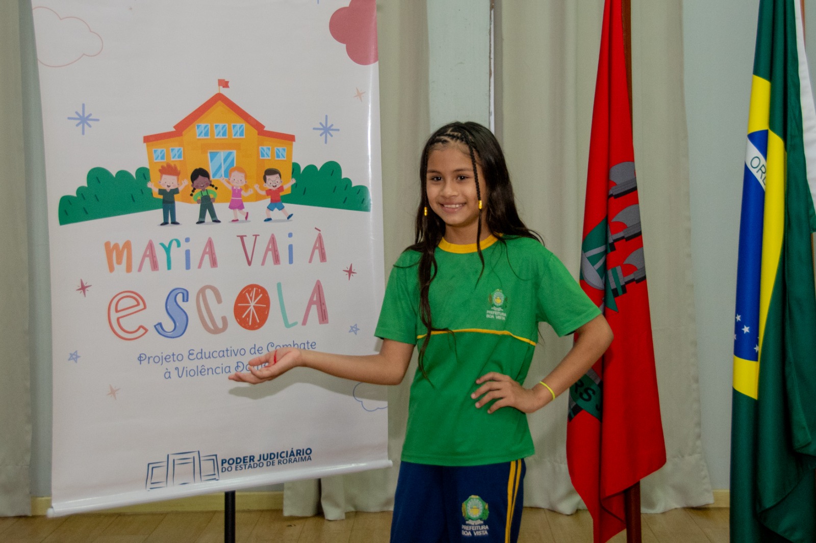 Foto colorida mostra uma criança estendendo a mão em direção a um banner do programa Maria Vai a Escola Foto 4: Foto colorida mostra uma criança estendendo a mão em direção a um banner do programa Maria Vai a Escola Foto 4: