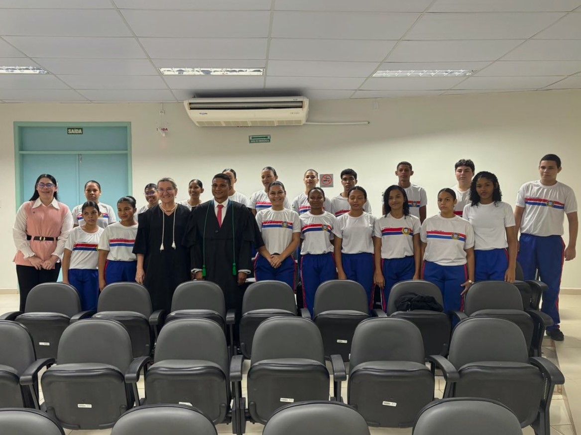A imagem mostra um grupo de pessoas posando para uma foto no auditorio da comarca de Alto Alegre. No centro da imagem está a juíza titular da unidade, Sissi Marlene, vestida com uma toga preta e branca. Ao redor há um grupo maior de jovens, estudantes, vestidos com uniformes escolares. A imagem mostra um grupo de pessoas posando para uma foto no auditorio da comarca de Alto Alegre. No centro da imagem está a juíza titular da unidade, Sissi Marlene, vestida com uma toga preta e branca. Ao redor há um grupo maior de jovens, estudantes, vestidos com uniformes escolares.