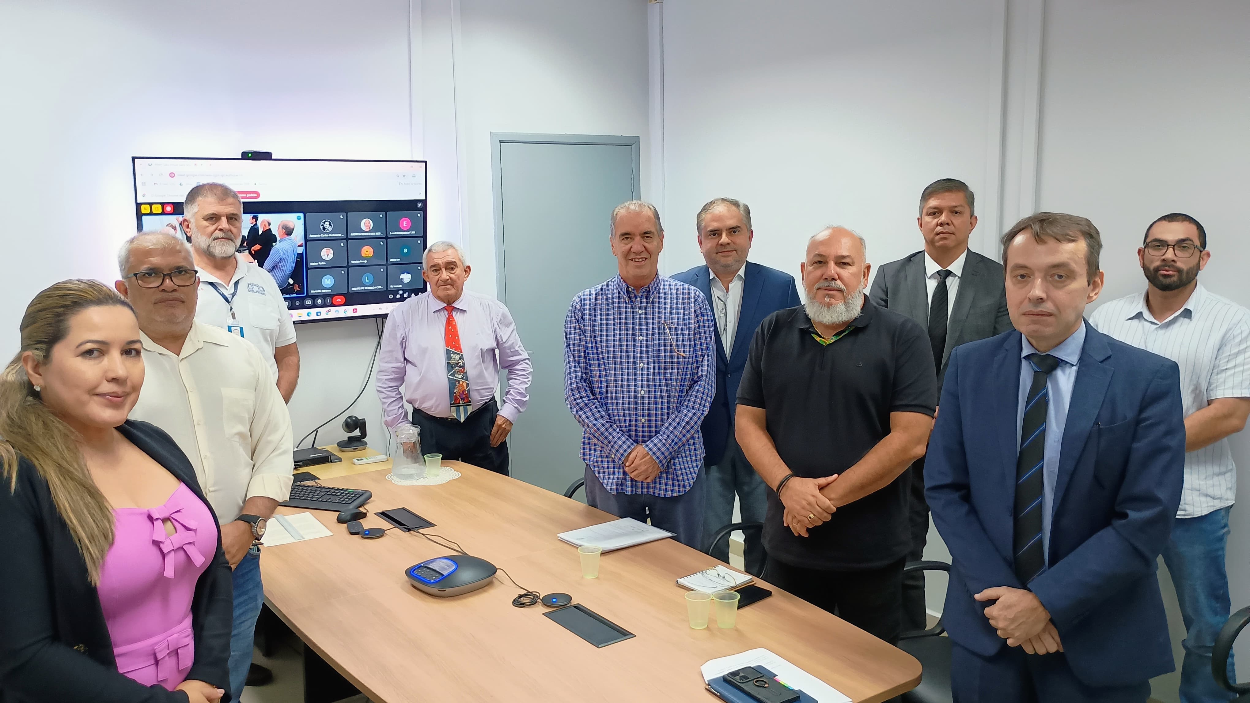 A imagem mostra um grupo de dez adultos posando para uma foto em uma sala de reuniões. Sendo nove homens e uma mulher. Na foto aparecem o Corregedor do Tribunal de Justiça de Roraima, Desembargador Erick Linhares, e o servidor da Corregedoria, Amadeu Triane.