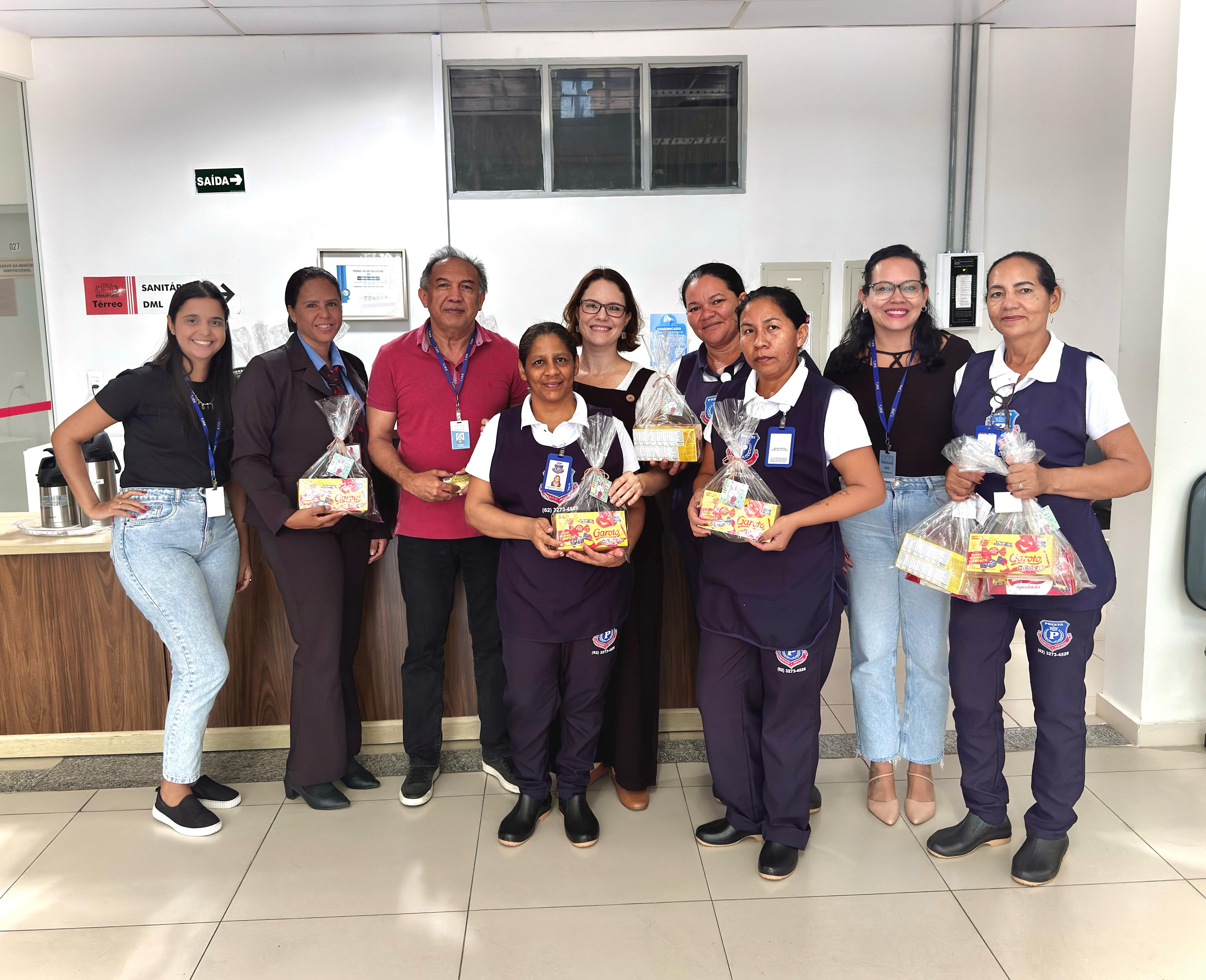 Foto colorida de 9 pessoas posando para fotografia. Nela há terceirizados e duas servidoras do setor SSRS Foto colorida de 9 pessoas posando para fotografia. Nela há terceirizados e duas servidoras do setor SSRS