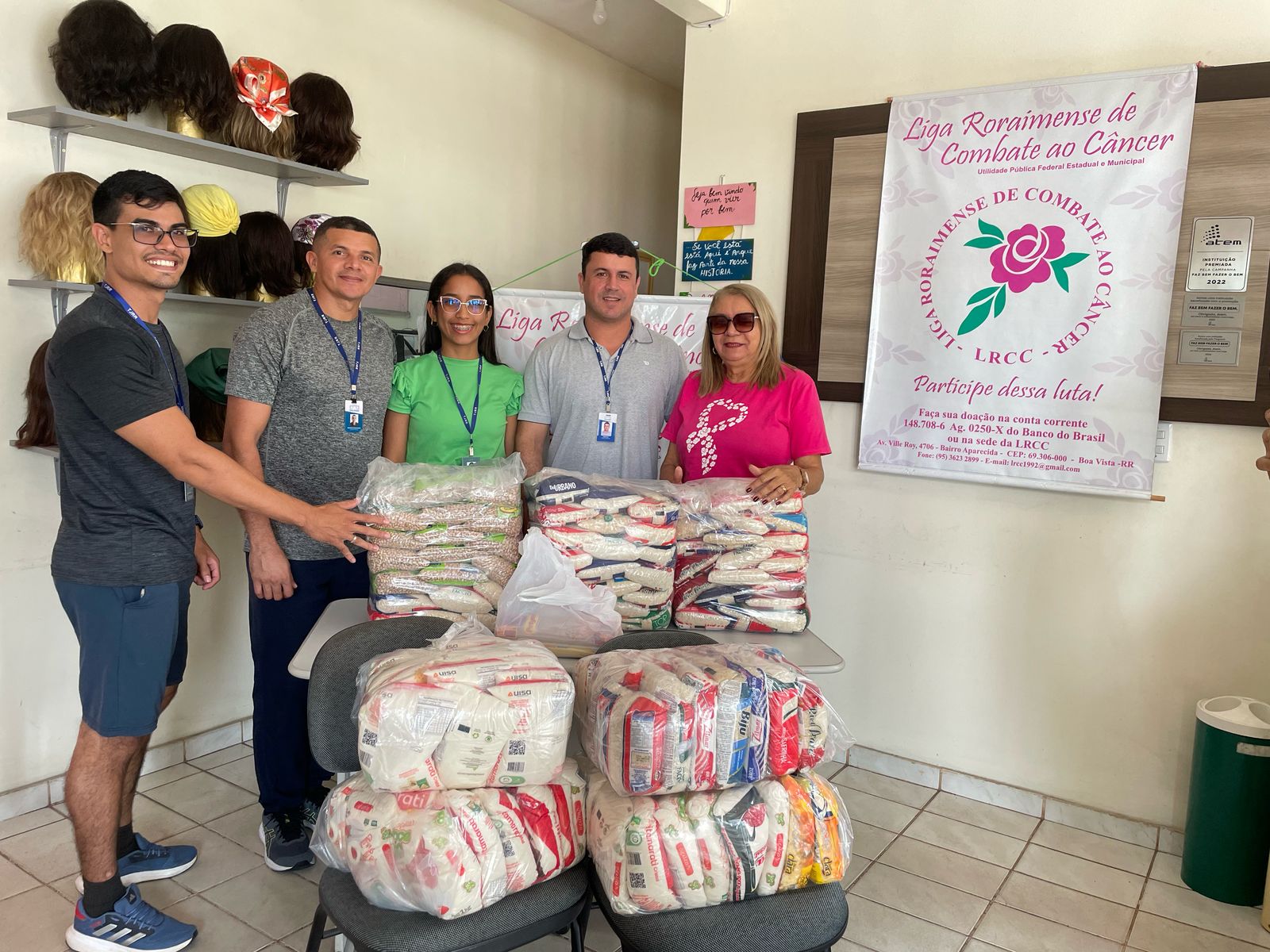 Foto colorida mostra cinco pesosas posando para foto na frente deles 7 fardos de alimentos não perecíveis Foto colorida mostra cinco pesosas posando para foto na frente deles 7 fardos de alimentos não perecíveis