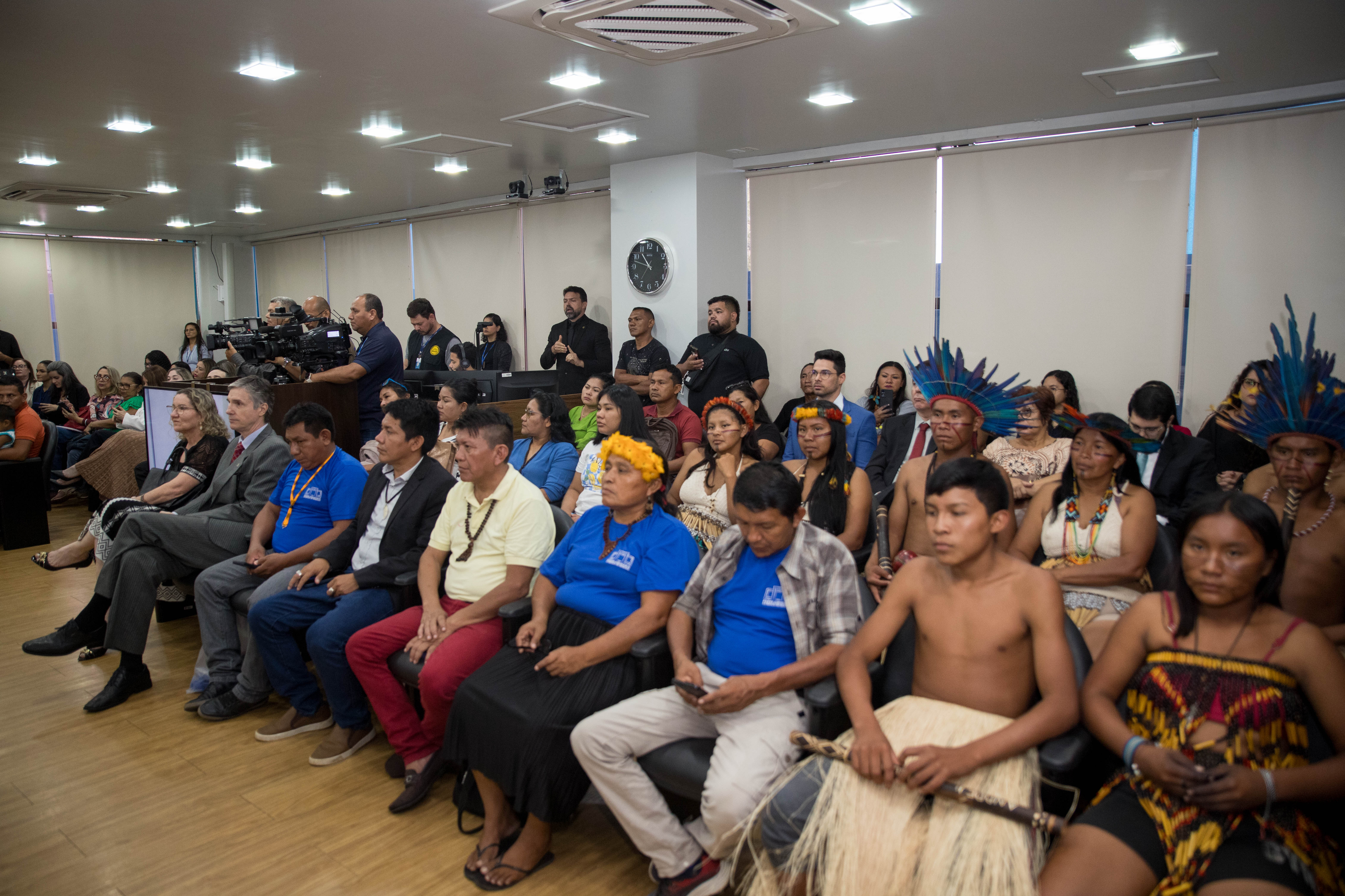  A imagem colorida mostra um grupo diversificado de pessoas sentadas Sala de Sessões do Tribunal Pleno. 