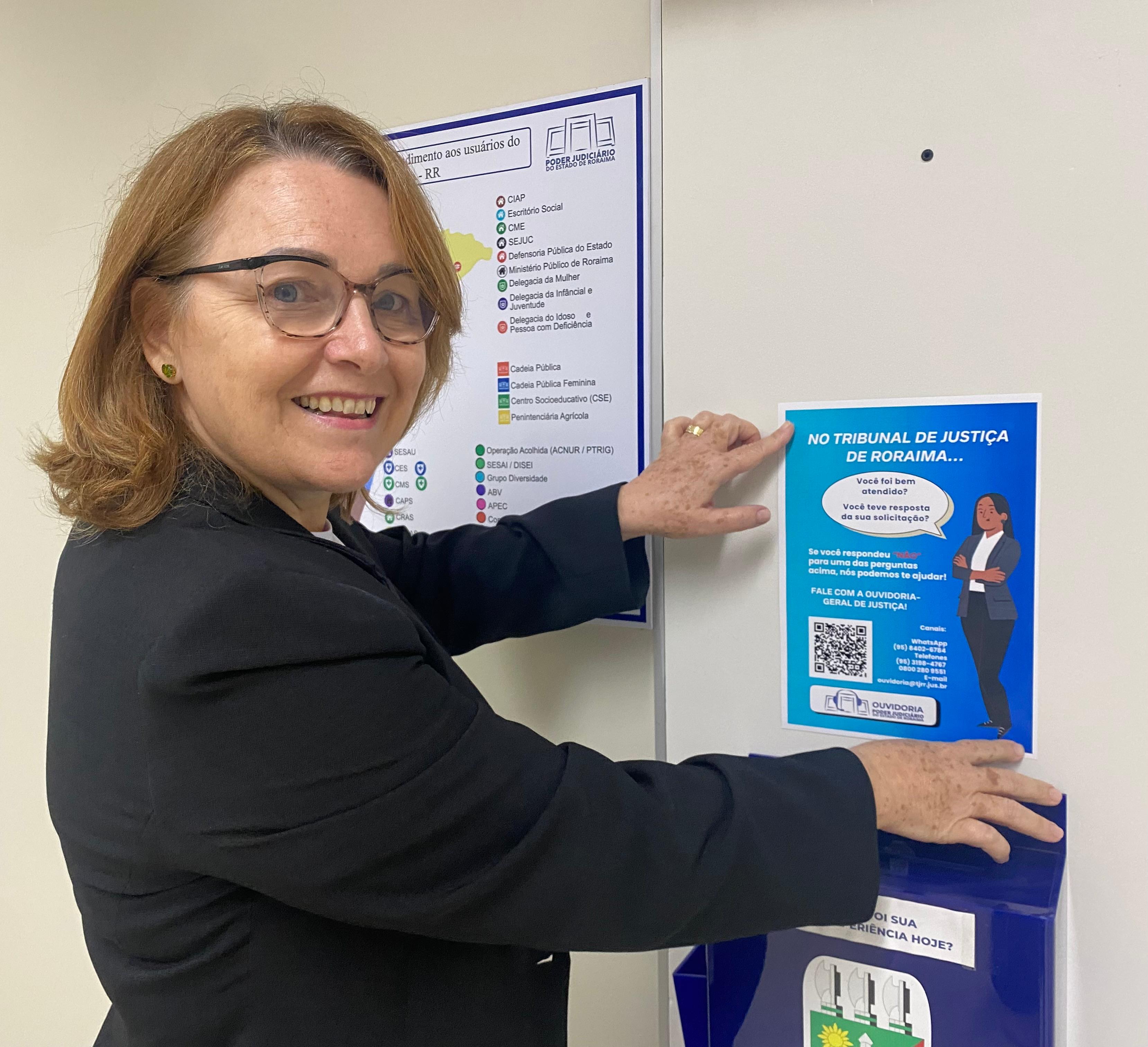Foto colorida mostra a Ouvidora-Geral de Justiça, Desembargadora Elaine Bianchi, colando um cartaz em uma parede. Foto colorida mostra a Ouvidora-Geral de Justiça, Desembargadora Elaine Bianchi, colando um cartaz em uma parede.
