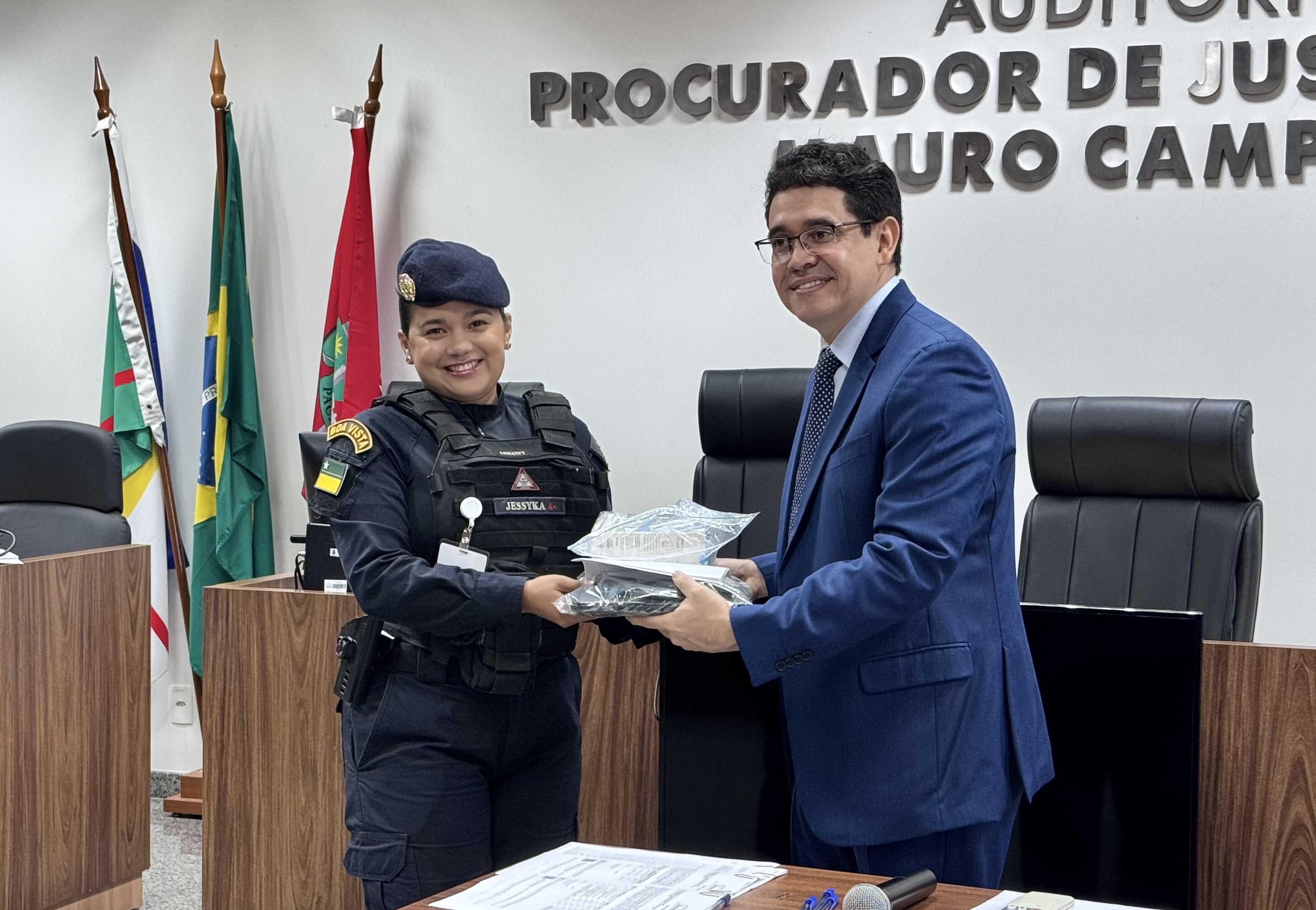 Imagem colorida de um homem entregando um saco transparente contendo os itens doados a uma representante da Patrulha Maria da Penha.
