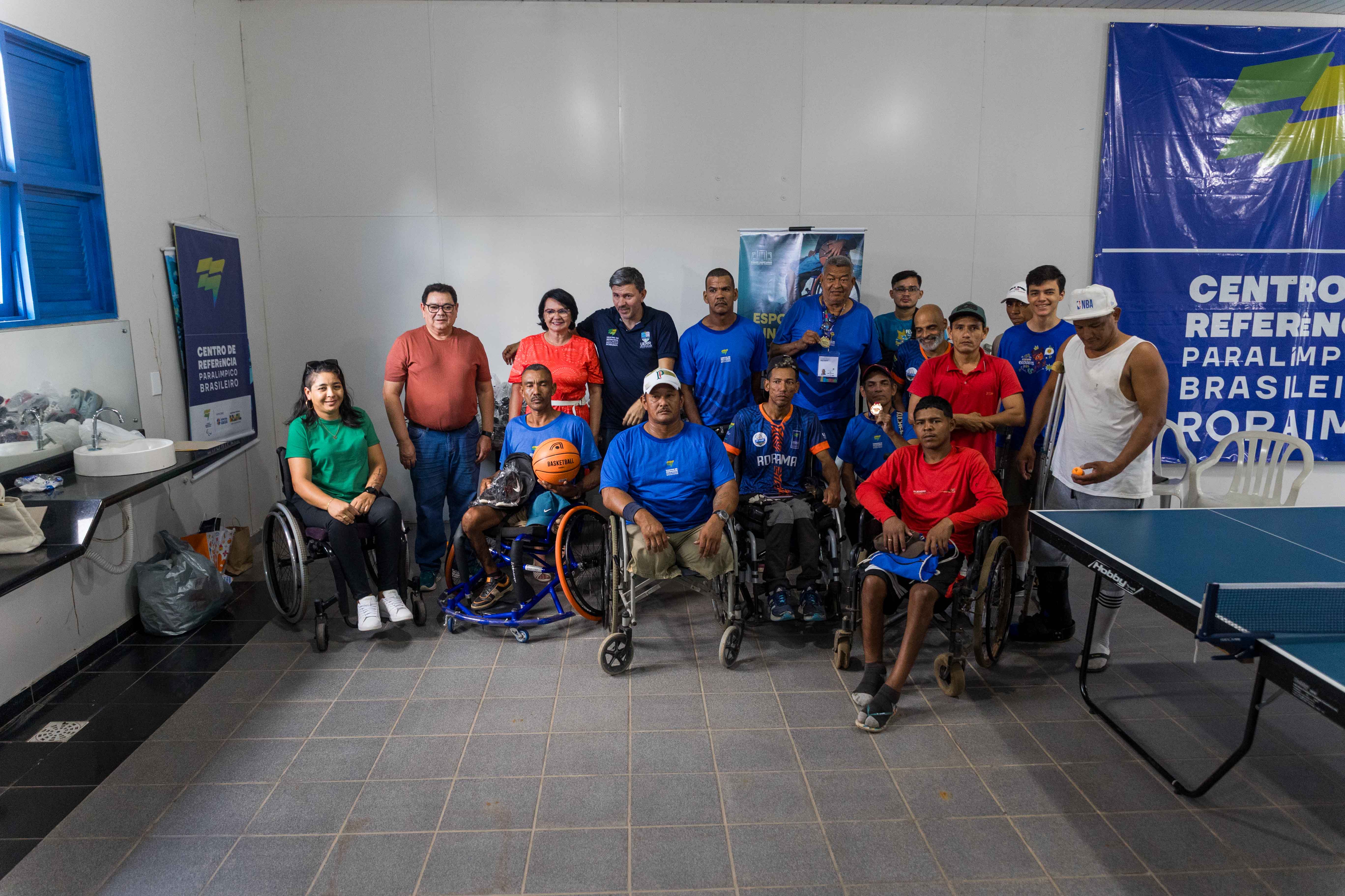 Foto colorida dividida ao meio mostra detalhes das pernas de dois atletas paralímpicos sentados em cadeiras de rodas esportivas azuladas. À esquerda, o atleta está descalço com uma bola de basquete no colo. À direita, o outro atleta usa tênis e boné, também com uma bola no colo.