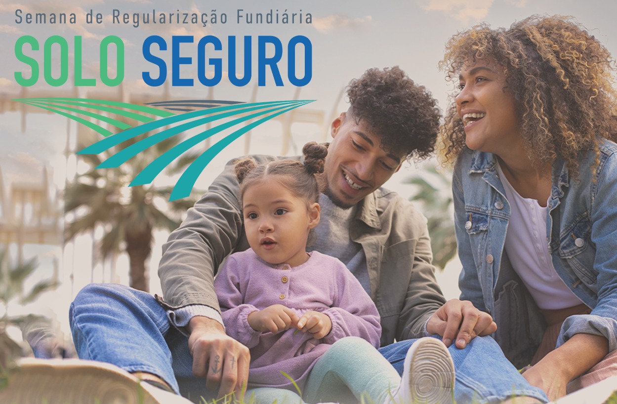 uma foto de uma família sorrindo, sentada na grama. Um homem de cabelo crespo e barba rala, uma mulher de cabelo cacheado e uma criança pequena de cabelo preso em dois coques. Eles olham para o lado direito da foto. A mulher e o homem seguram as mãos da criança. No topo da foto há um texto com a frase Semana de Regularização Fundiária e logo abaixo o slogan SOLO SEGURO, com um desenho de linhas curvas em tons de azul e verde que se assemelham a um campo de terra. uma foto de uma família sorrindo, sentada na grama. Um homem de cabelo crespo e barba rala, uma mulher de cabelo cacheado e uma criança pequena de cabelo preso em dois coques. Eles olham para o lado direito da foto. A mulher e o homem seguram as mãos da criança. No topo da foto há um texto com a frase Semana de Regularização Fundiária e logo abaixo o slogan SOLO SEGURO, com um desenho de linhas curvas em tons de azul e verde que se assemelham a um campo de terra.