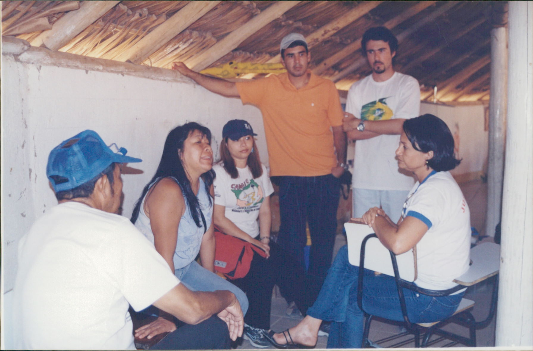 Imagem colorida mostra um grupo de seis pessoas reunido sob um telhado de palha. Três mulheres e três homens estão em círculo conversando, entre eles a desembargadora Tânia Vasconcelos.